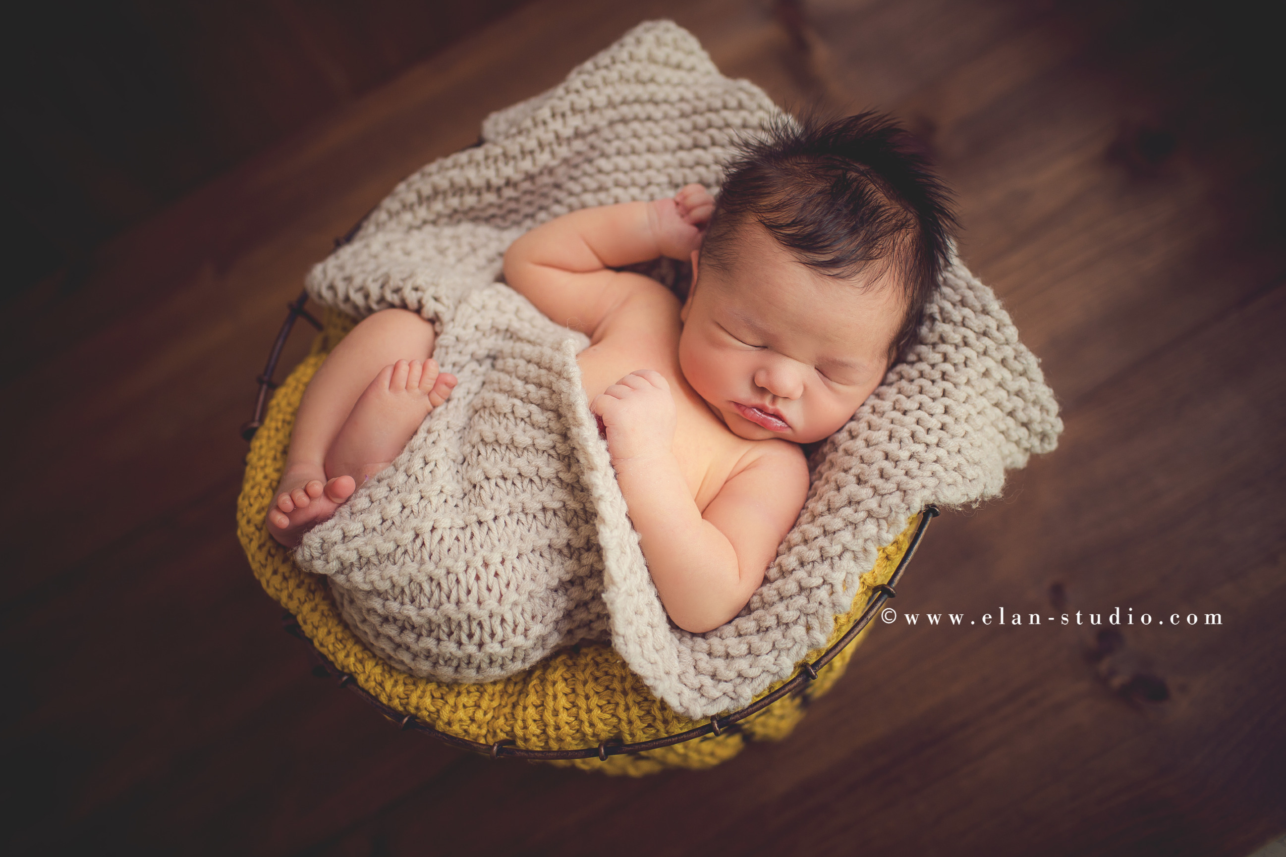 newborn baby with lots of hair, wrapped in oatmeal and mustard, in basket