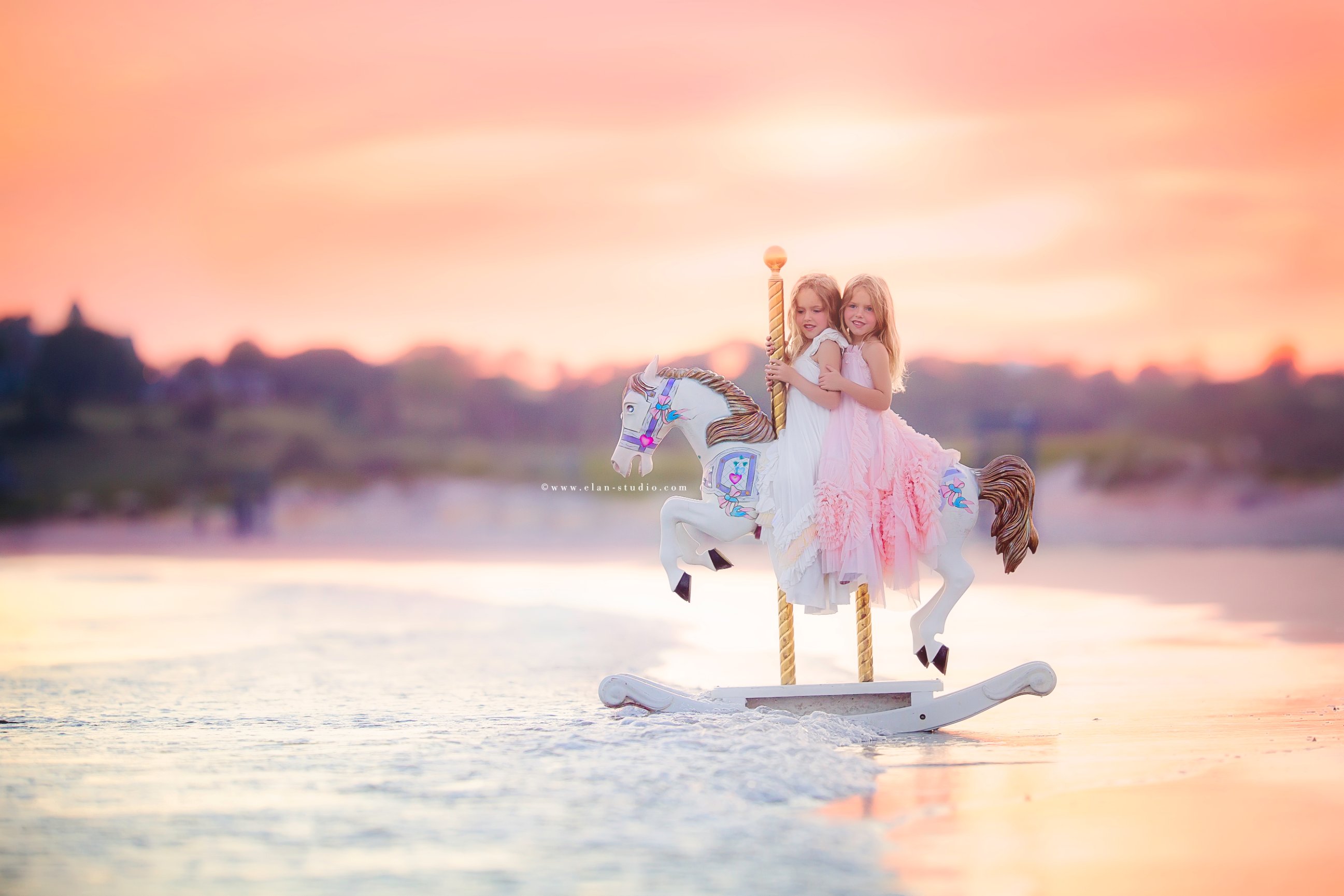 two little girls riding a unicorn rocker in the ocean