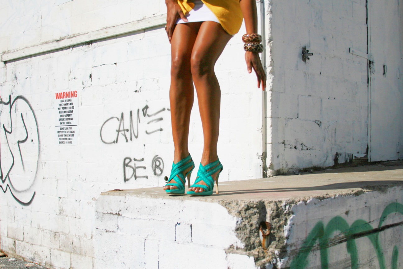 Woman standing on a concrete ledge wearing turquoise high heels.