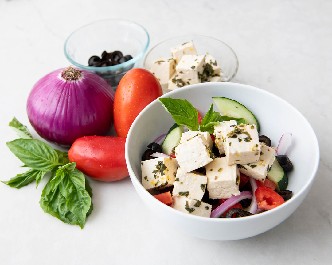 Fresh salad with cubes of feta cheese, cucumbers, tomatoes, red onion, black olives, and basil.