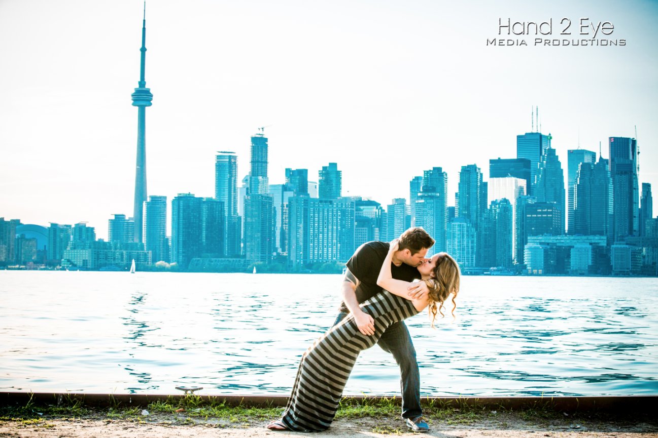 Couple kissing by waterfront with Toronto skyline and CN Tower in background.