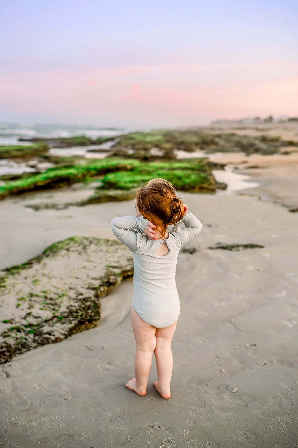 little girl staring out at rocky, mossy coastline, Florida, Ryaphotos