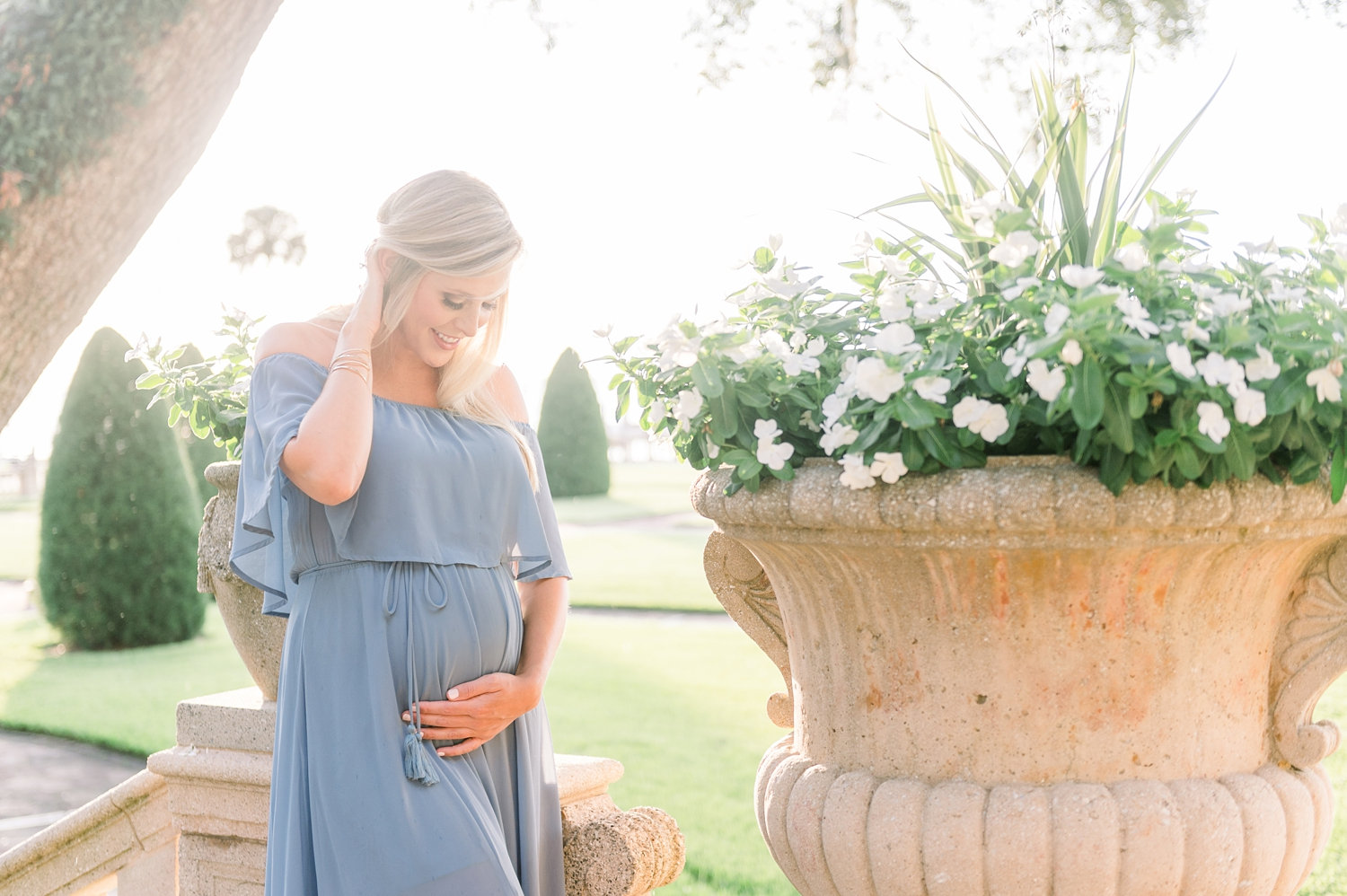 mom to be smiling down at her baby bump, she is tucking her long blonde hair behind her ear with one hand and holding her pregnant belly with the other, sunset maternity photo