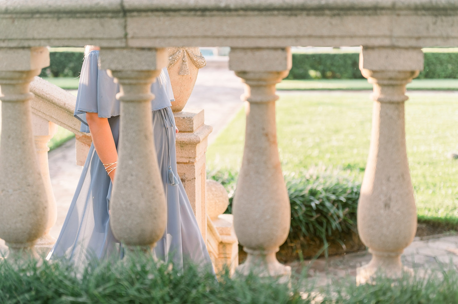 peek at a walking pregnant woman through stone architectural columns in a manicured garden