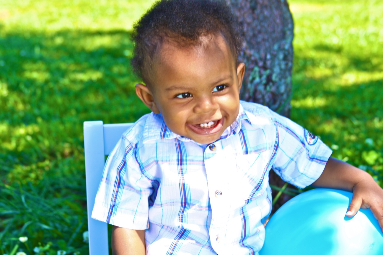 Smiling toddler sitting outdoors next to a blue balloon.