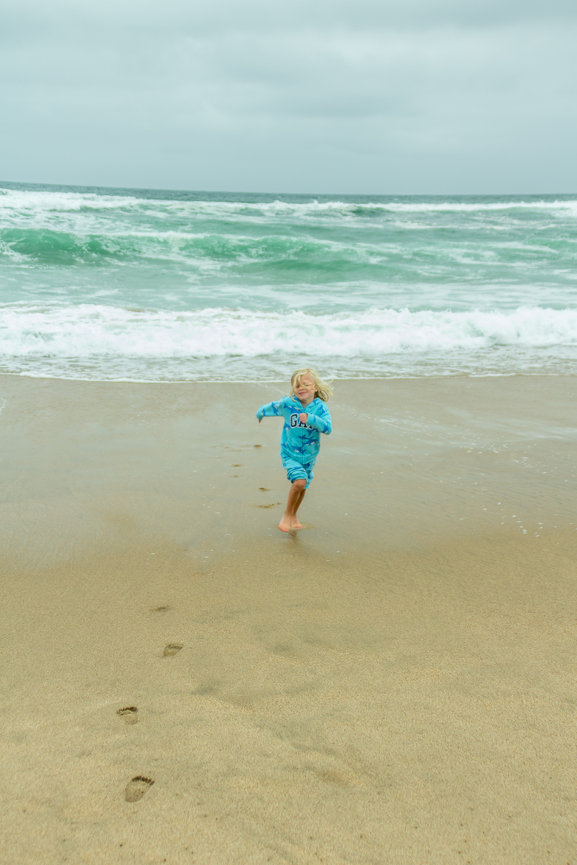 Child running on a sandy beach near the ocean waves under a cloudy sky