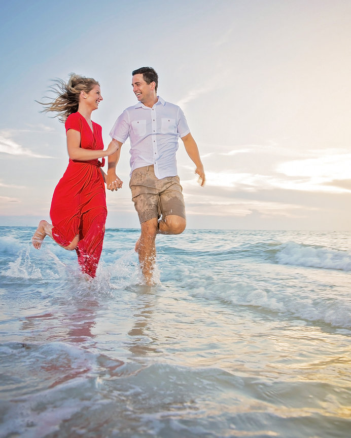 Couple joyfully running hand in hand through shallow ocean water at sunset.