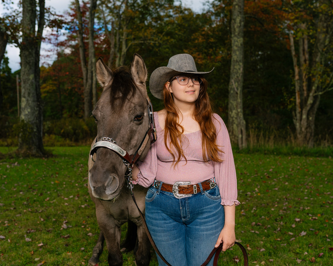 senior girl with horse wearing a pink shirt, jeans and cowboy hat