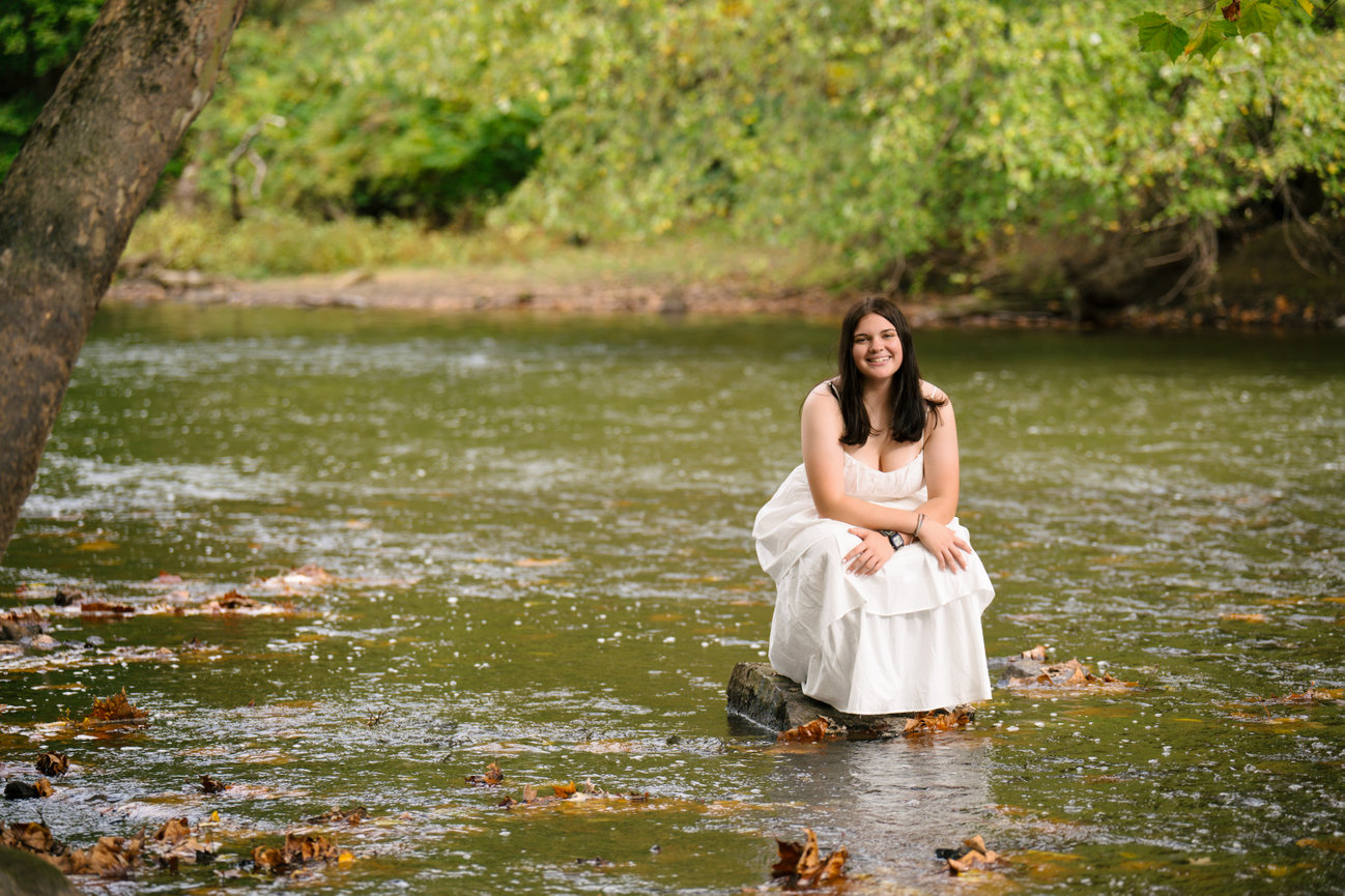 high school senior wearing a white flowy dress in a river during her senior pictures