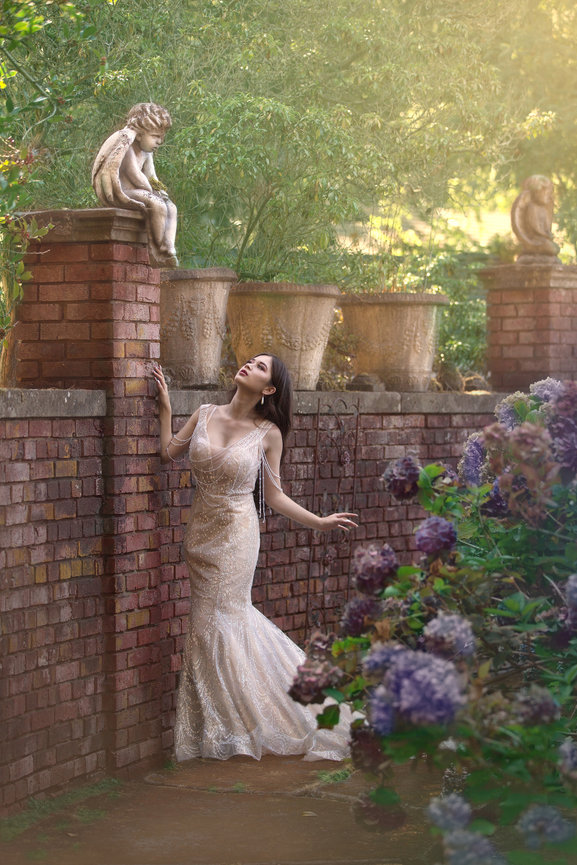 Woman in a gown posing by a brick wall with ivy and statues
