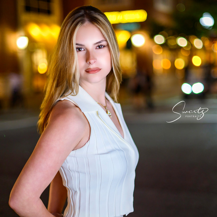 Class of 2027 senior portrait of blonde girl in white ribbed knit collared crop top with gold pendant, urban evening bokeh background in The Woodlands, contemporary editorial fine art by Ty Swartz, Swartz Portraits Spring Texas
