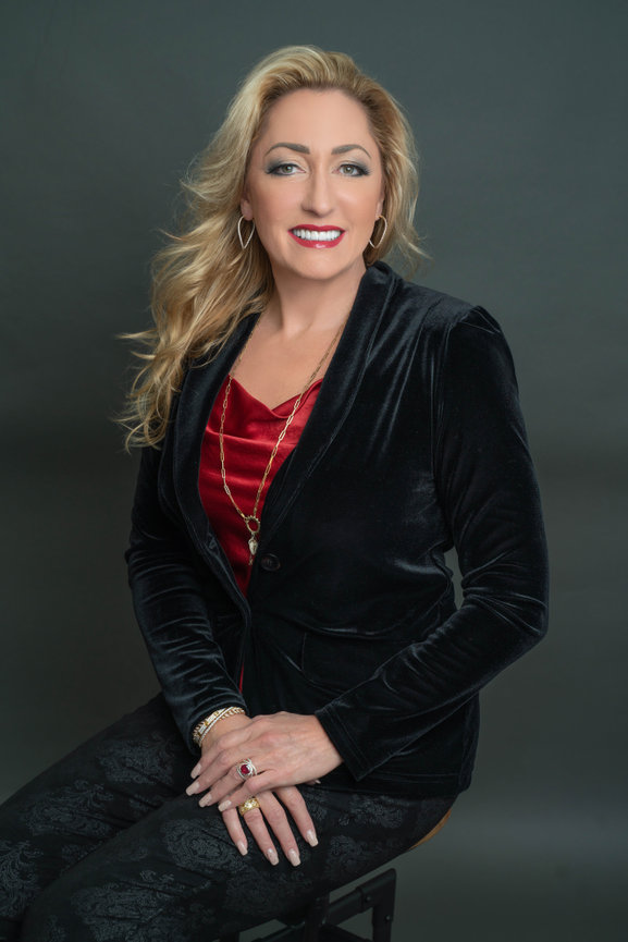 Woman in black jacket with red top, seated and smiling for a branding photo.