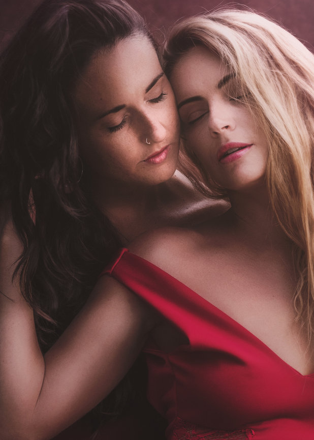 Two women with closed eyes pose closely together in a soft studio Fine Art Painterly Portrait , one wearing a red dress.