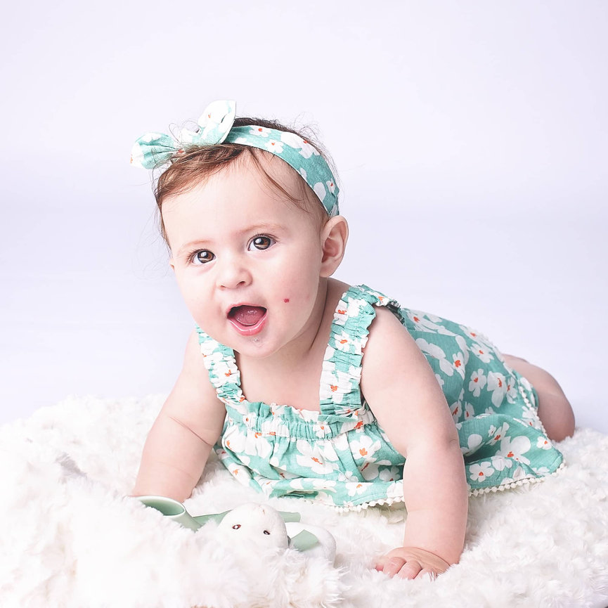 A drooling six month old girl in a daisy dress pushes up on her hands and knees