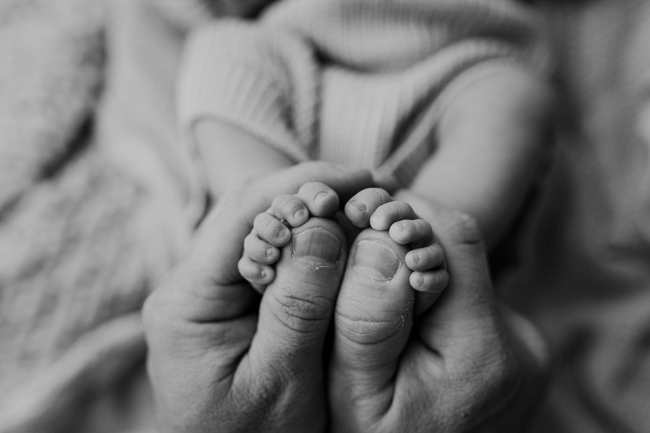close up of newborn toes with dads holding them