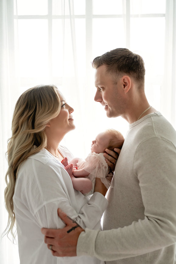 New parents holding their newborn baby in a bright window-lit room