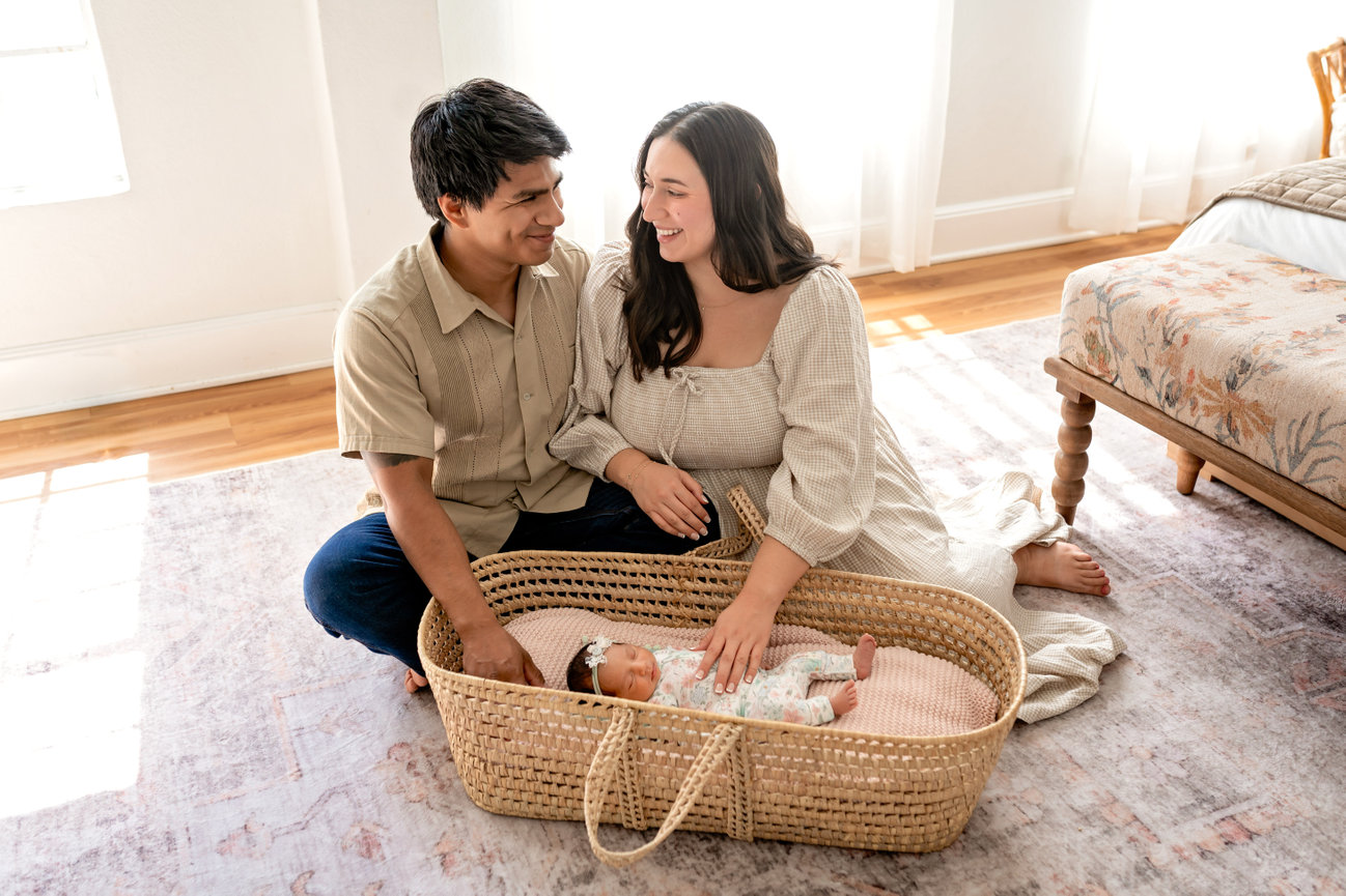 New parents smiling at their newborn in a wicker basket in a sunlit bedroom