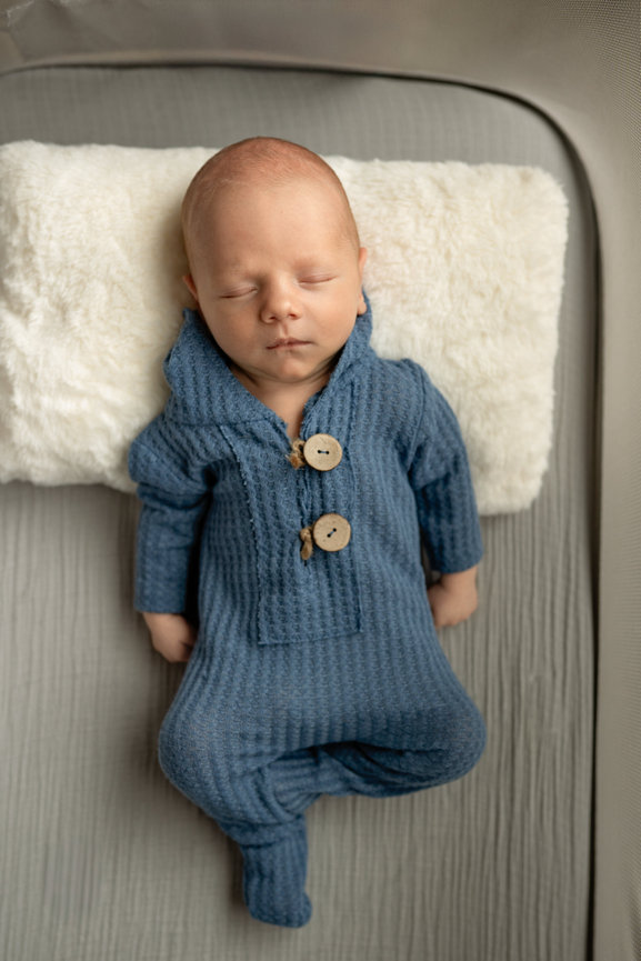 Sleeping newborn baby in a blue knit outfit lying on a soft white pillow