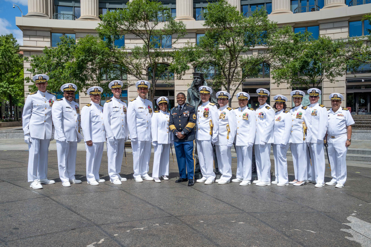 A group of Naval Officers and one Army enlisted posing in front of the Lone Sailor at the Navy Memorial in Washington DC