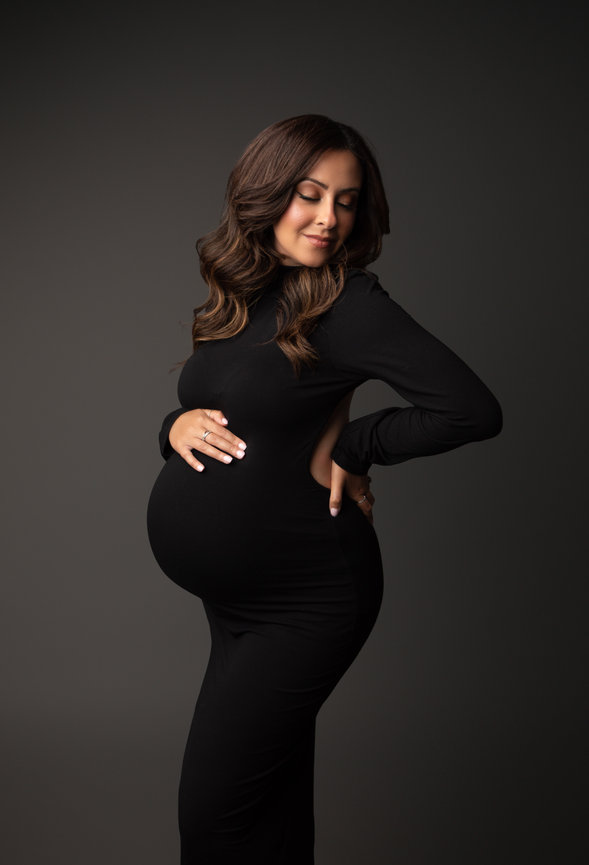 Pregnant woman in a black dress posing against a dark background.