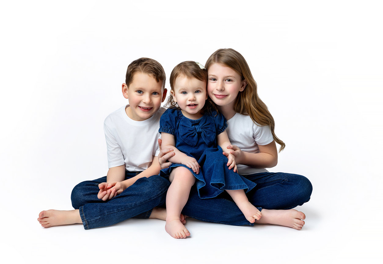 Three siblings smiling together during a children's portrait session at Elle Lux Studios.