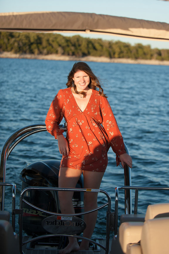 pretty senior girl in orange dress standing on boat for portrait at Branson Missouri