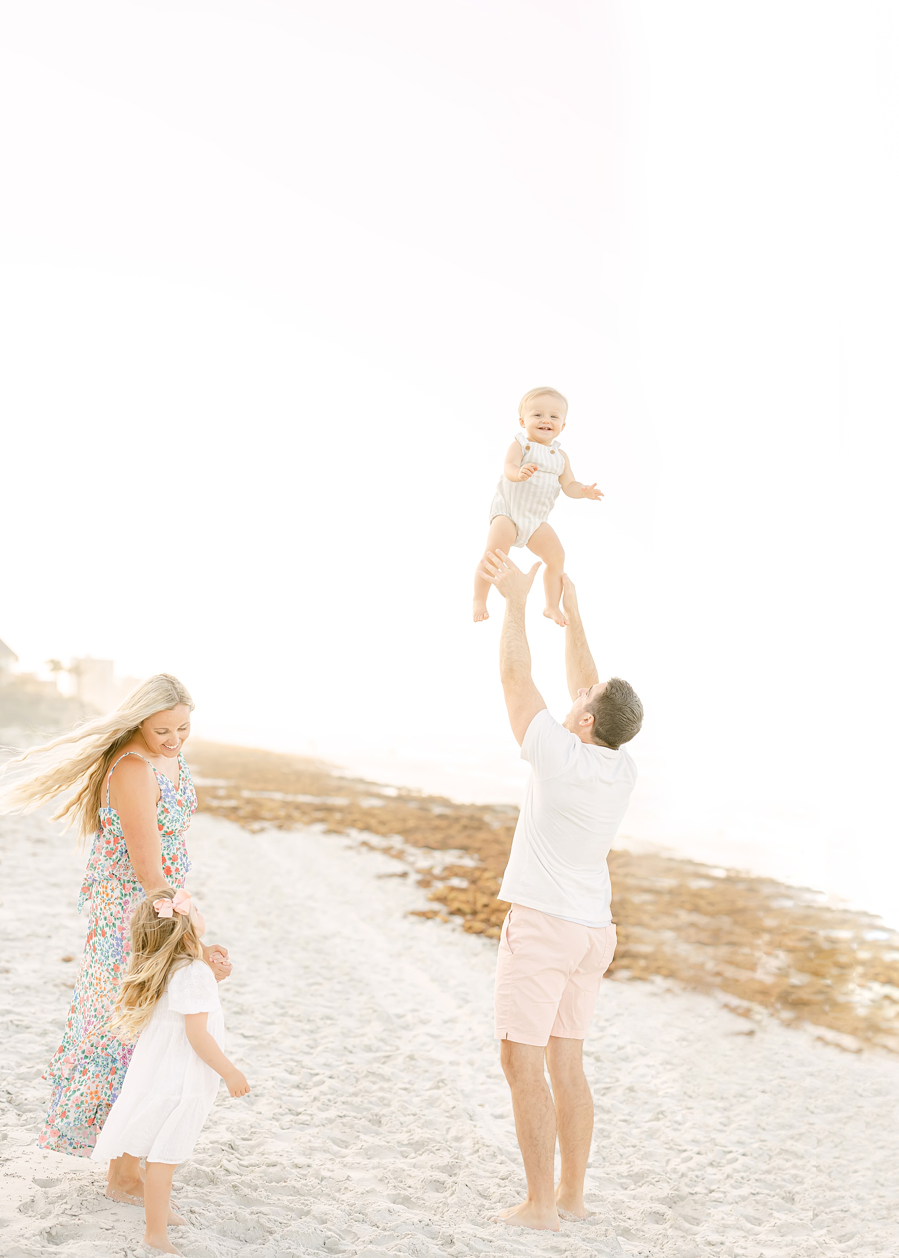 family throwing baby in the air on the beach light and airy look