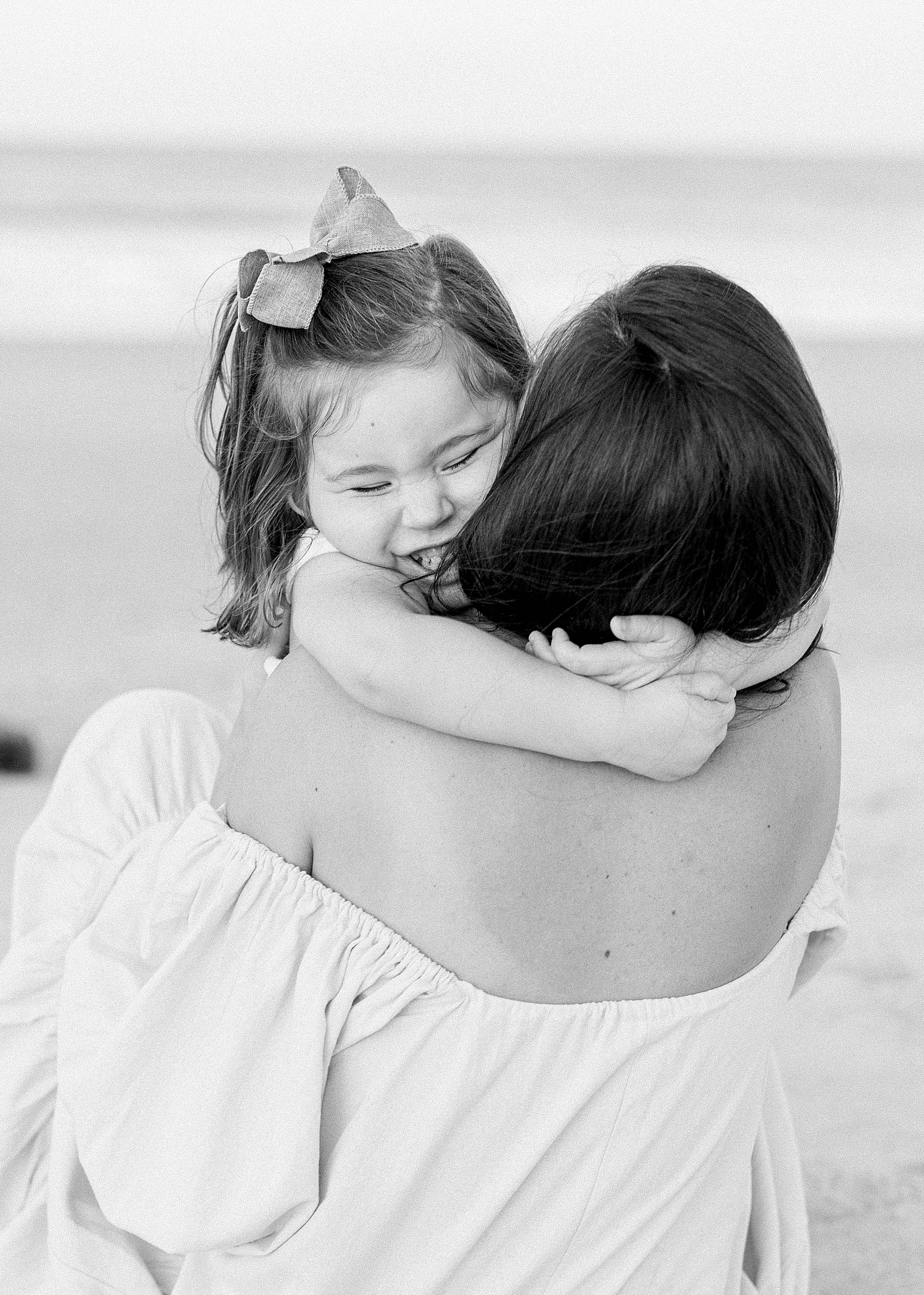 little girl kissing and smiling with her mom on the beach