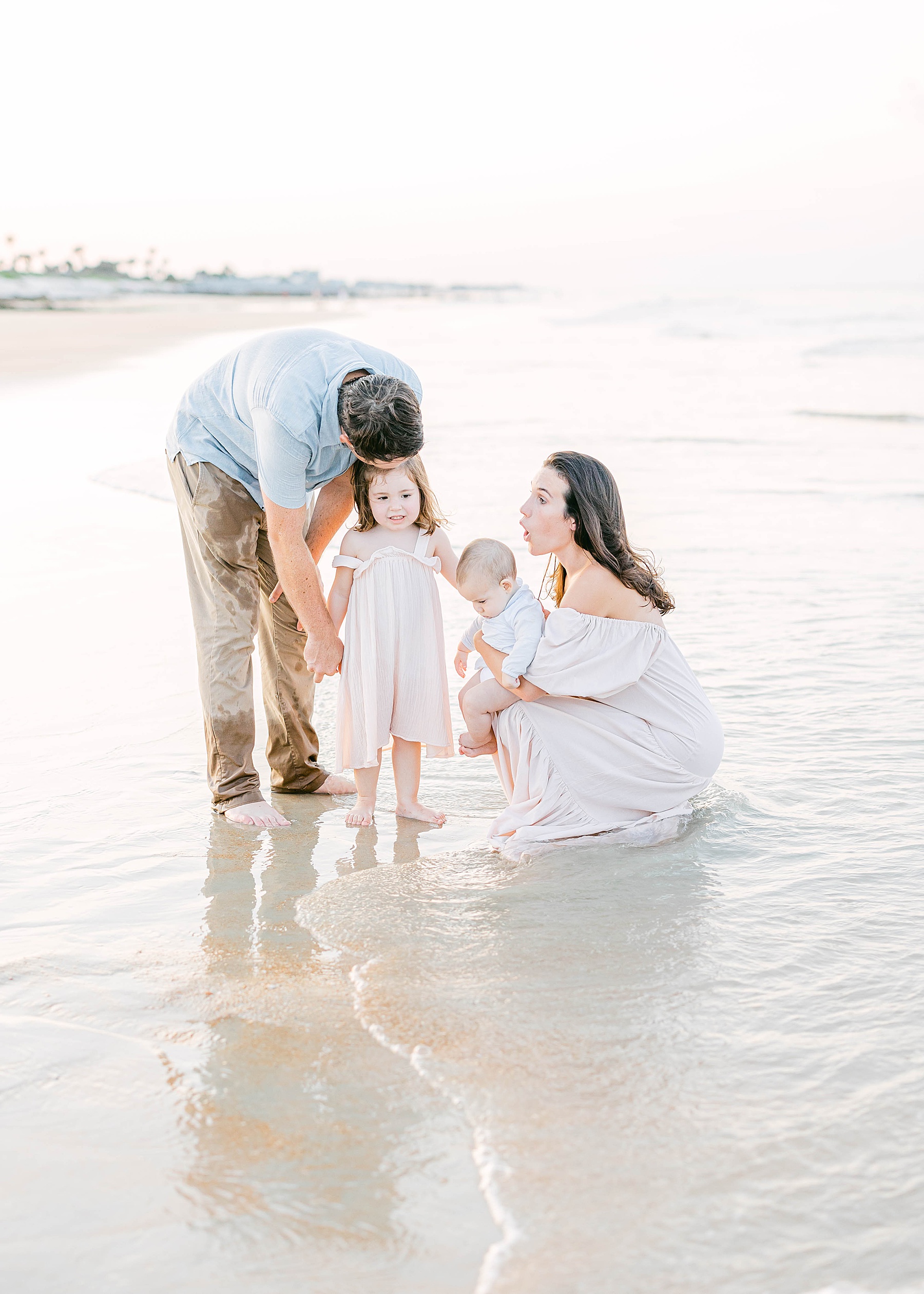 family standing together along the shoreline at sunset wearing pastel colors