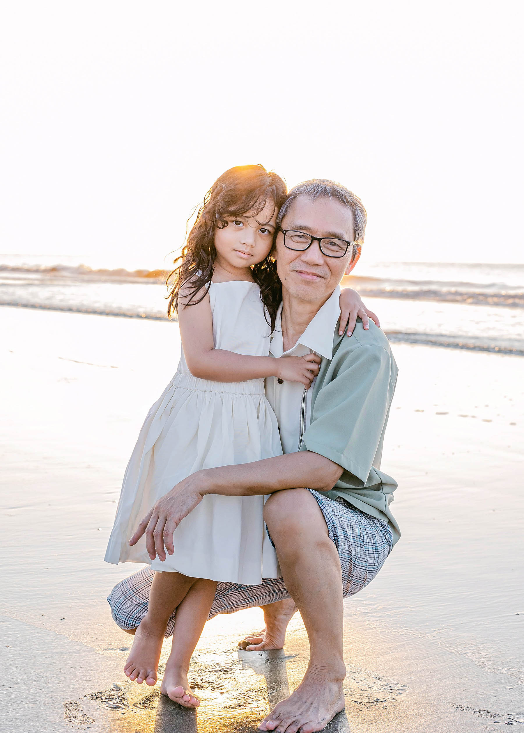 old man holding young girl in white dress at sunrise on the beach