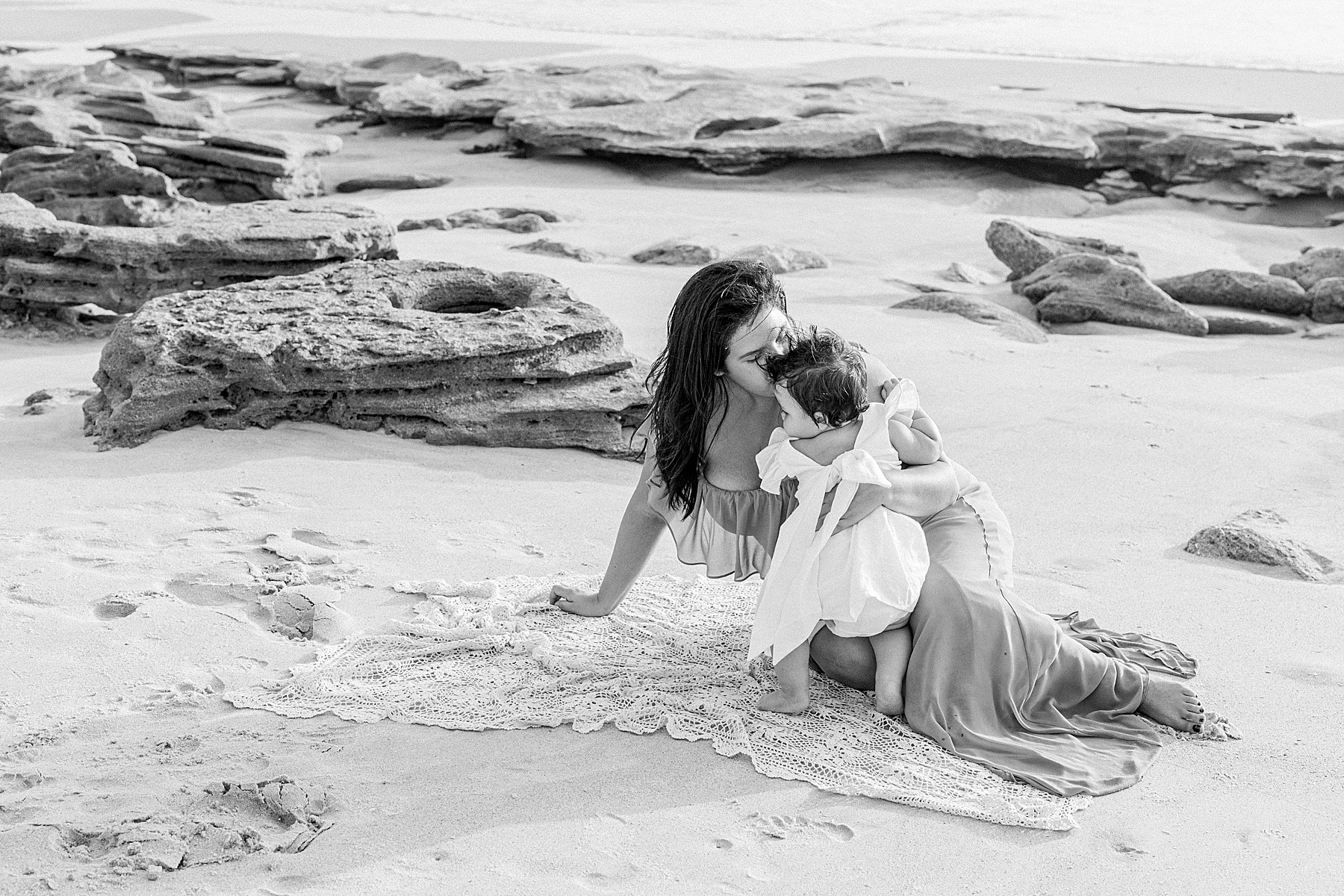 woman in blue dress holding baby girl wearing white on the beach