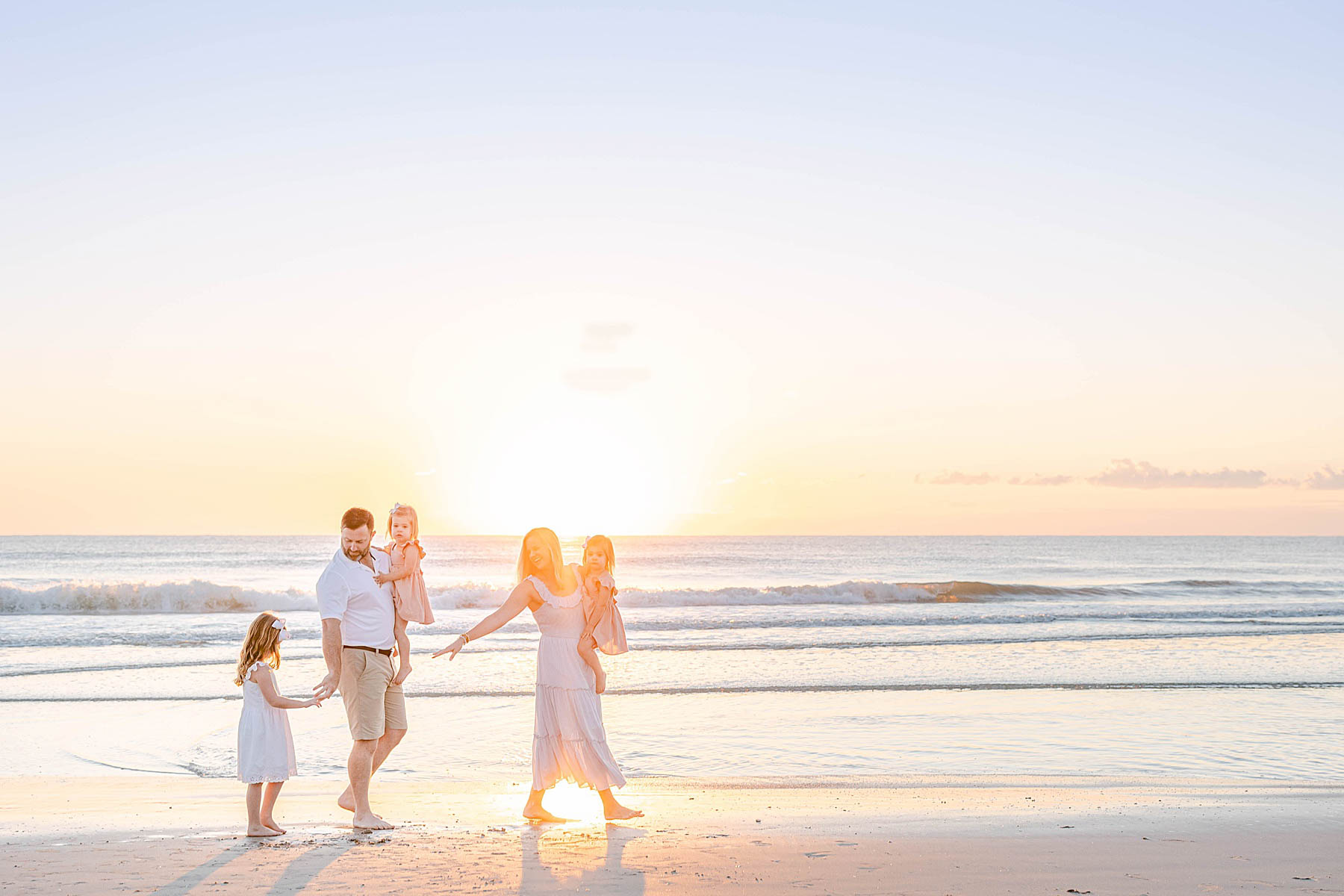 family on the beach at sunrise wearing pastel colors