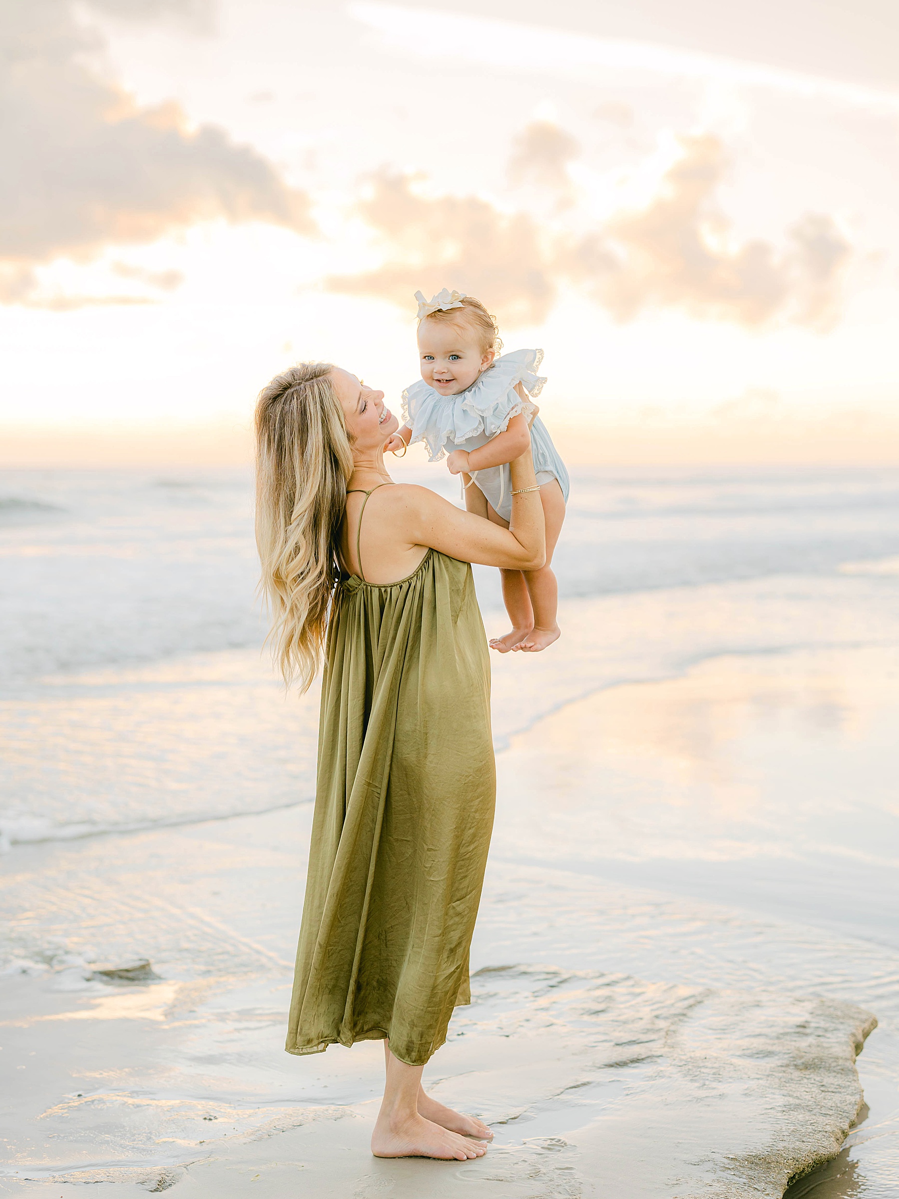 woman snuggling baby girl wearing blue outfit at the beach at sunrise