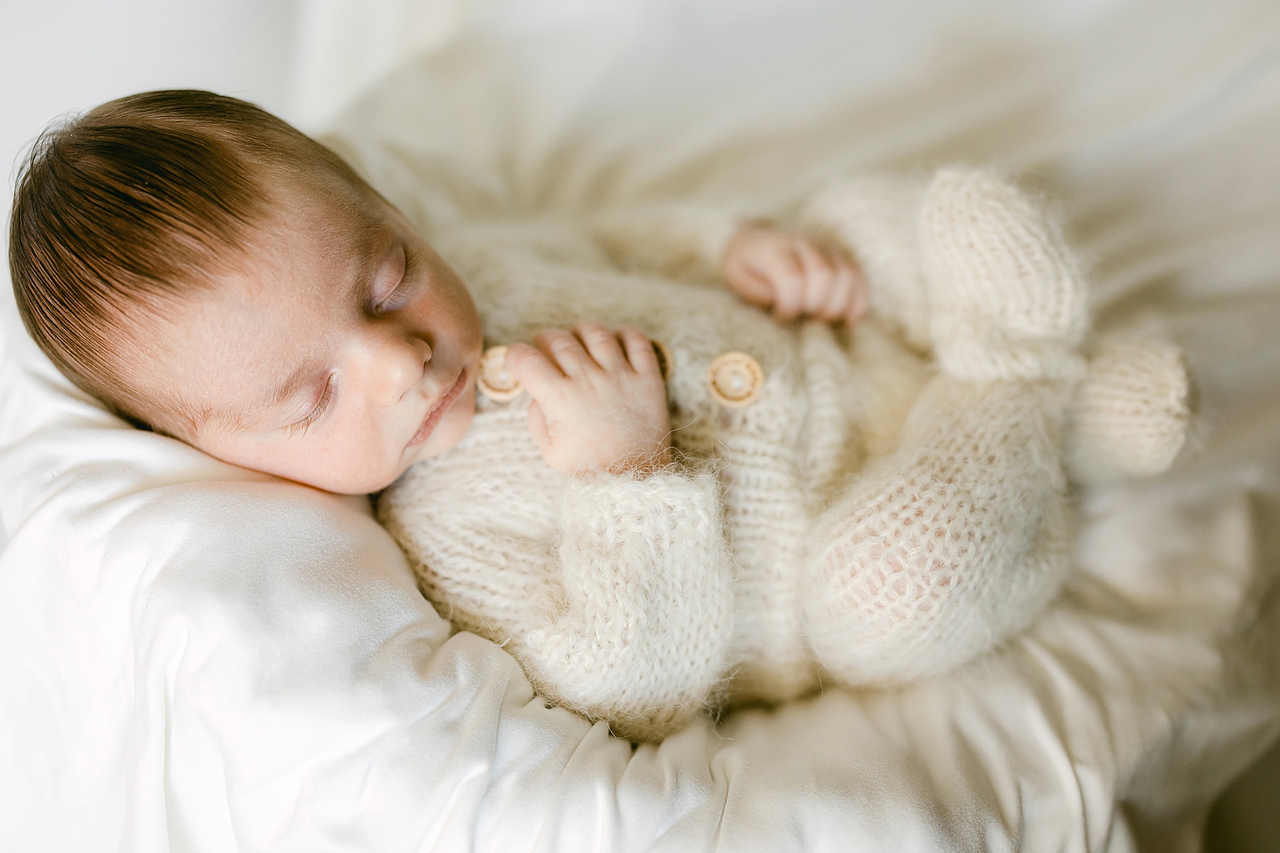 newborn baby wearing a wool outfit sleeping in bucket with white blankets