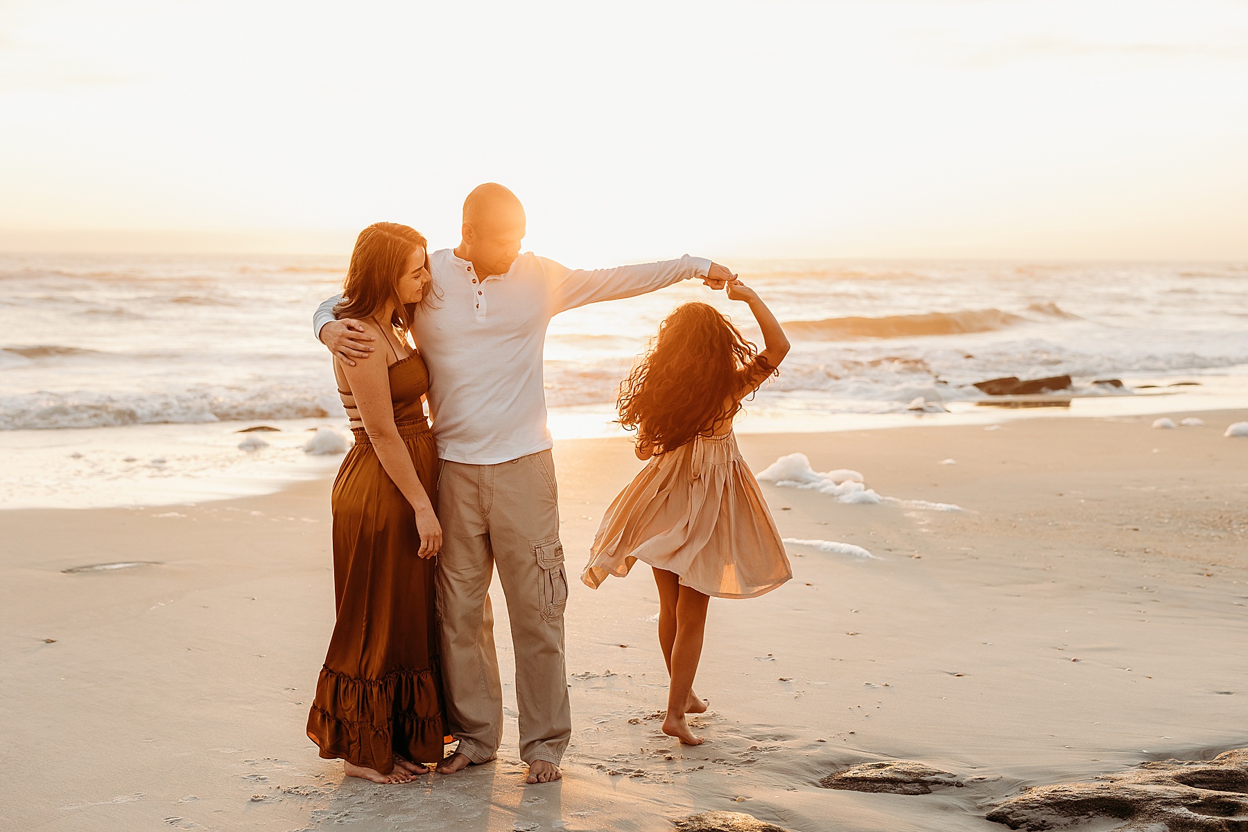 family standing and laughing at sunrise on the beach 