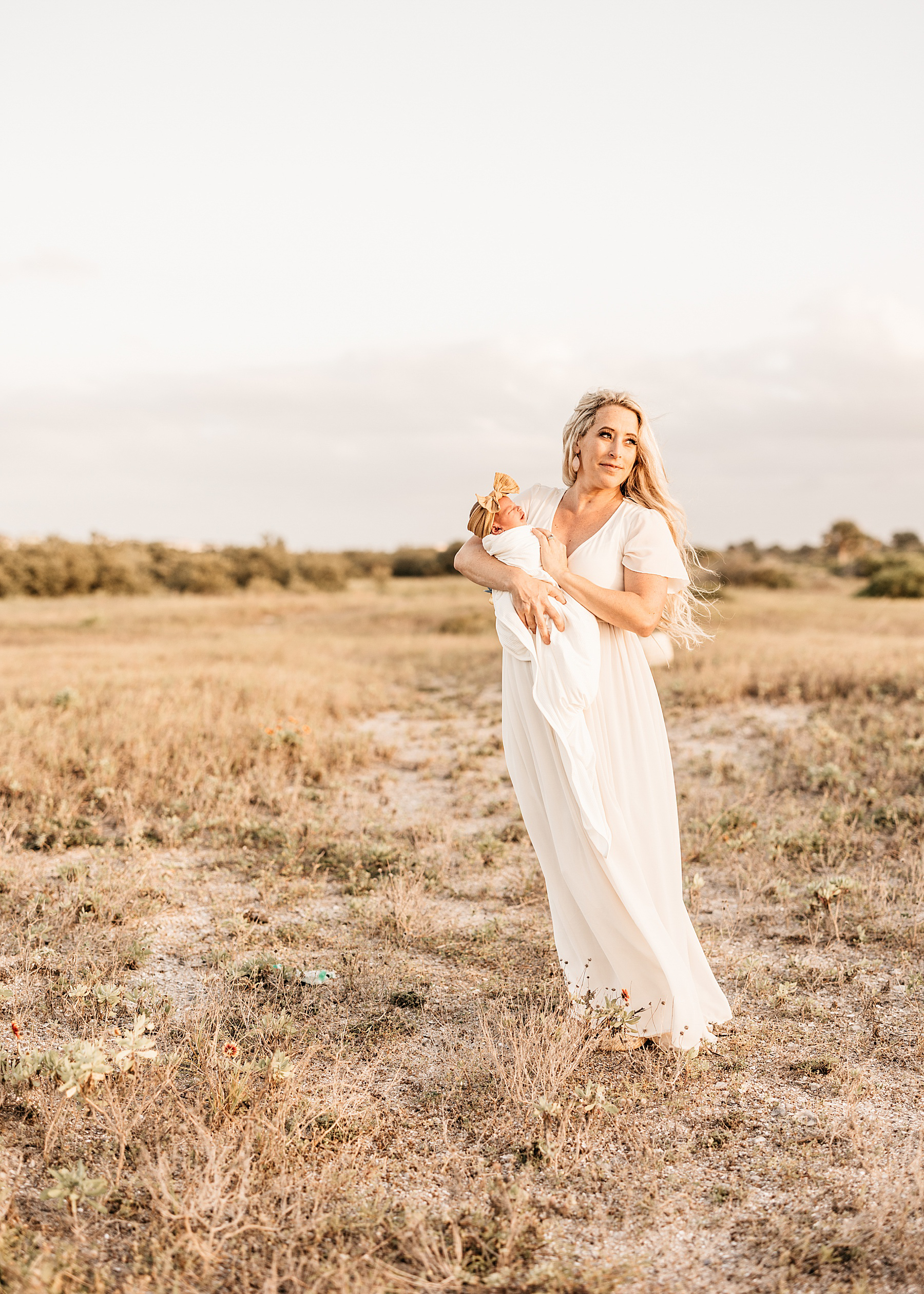 woman wearing cream maxi dress holding baby boy wrapped in neutral swaddle