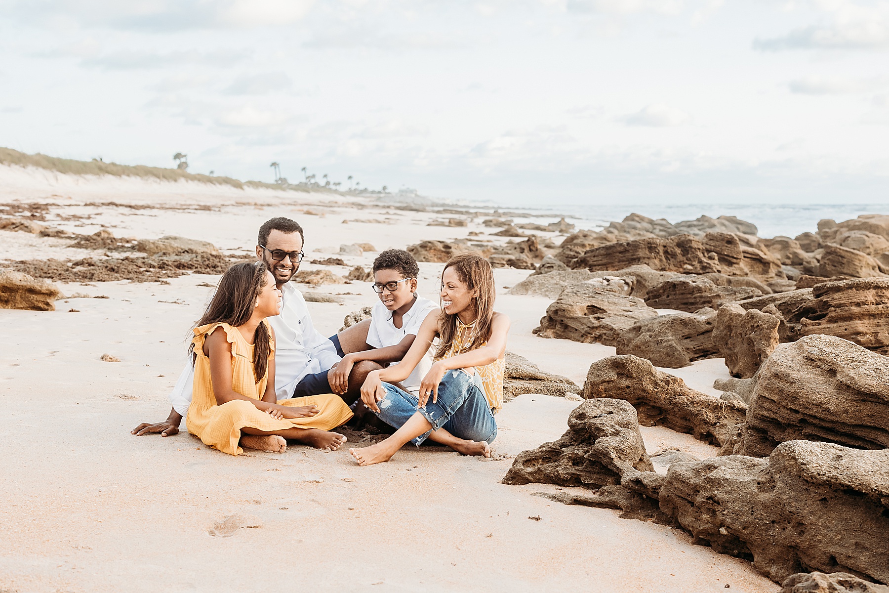 family of four sitting on the beach talking together at sunrise