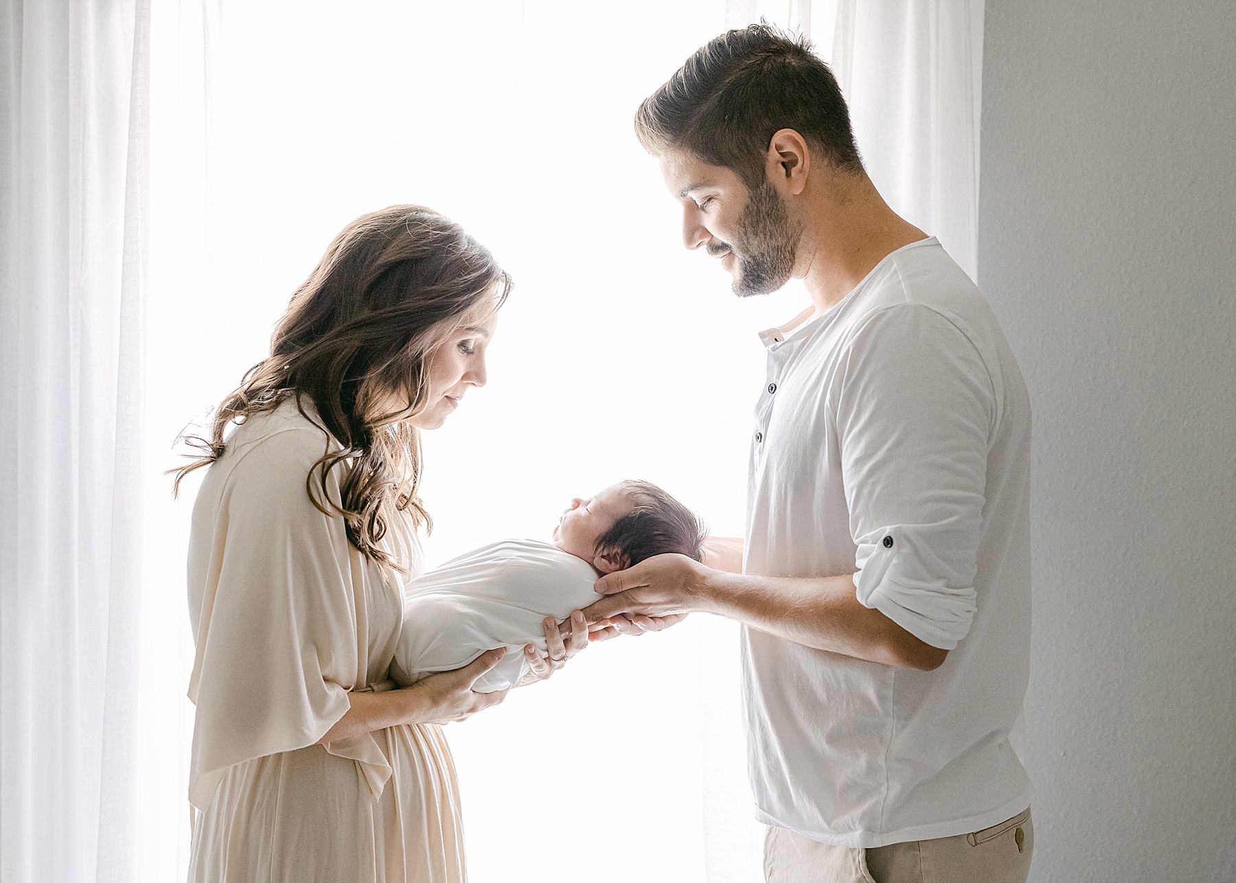 backlit light and airy image of couple holding newborn baby boy in bright white light