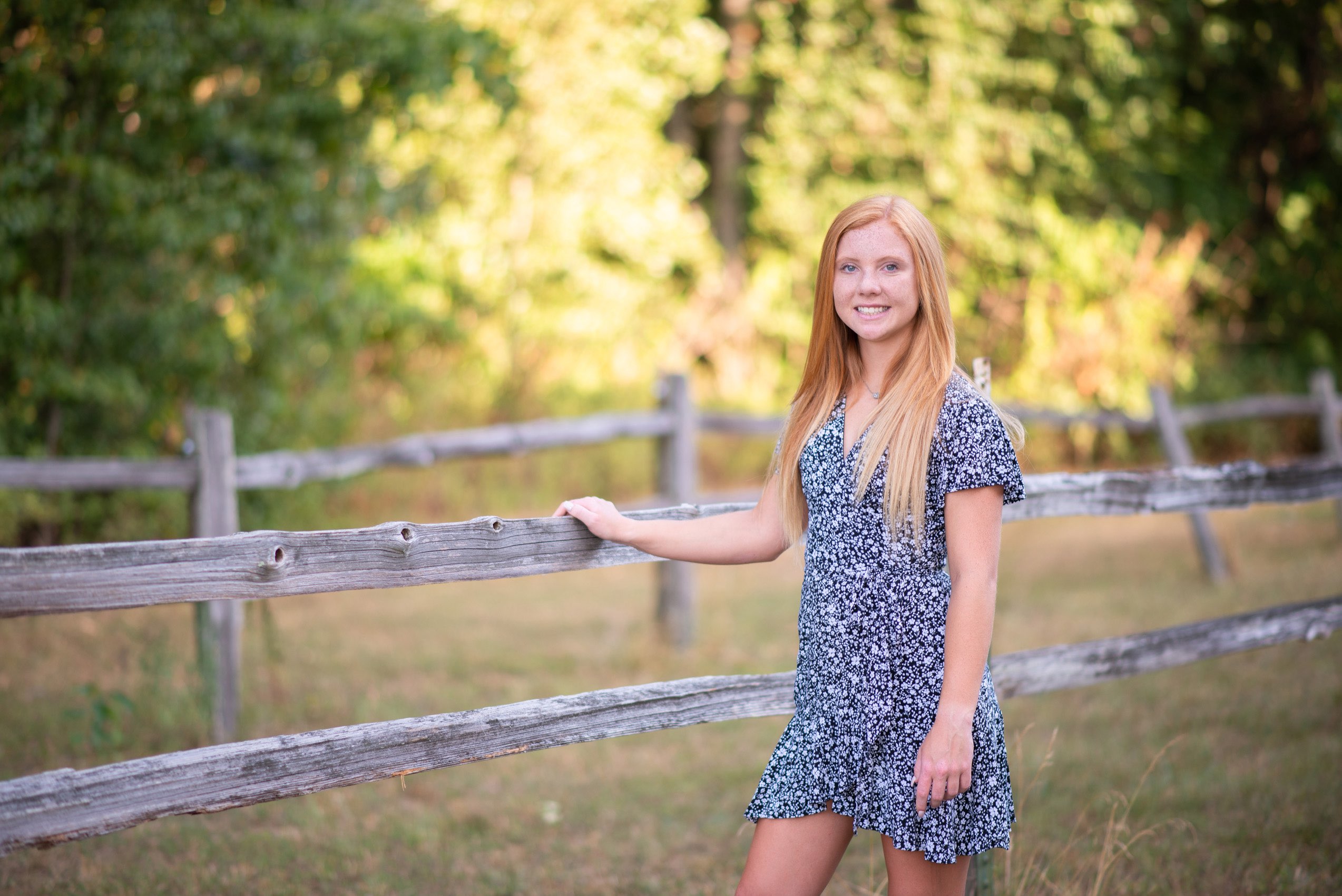 Senior girl in print dress in front of a fence in Reeds Spring, Missouri.