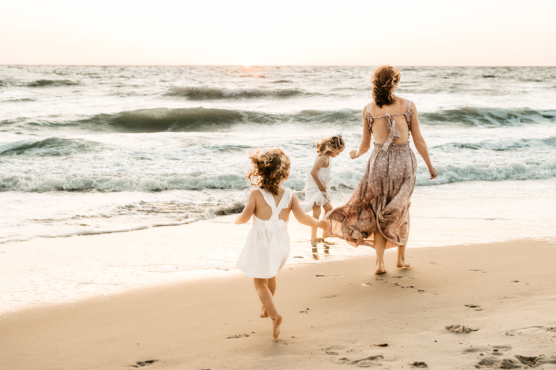 woman in long dress standing at the shoreline at sunset in Naples, Florida with her children