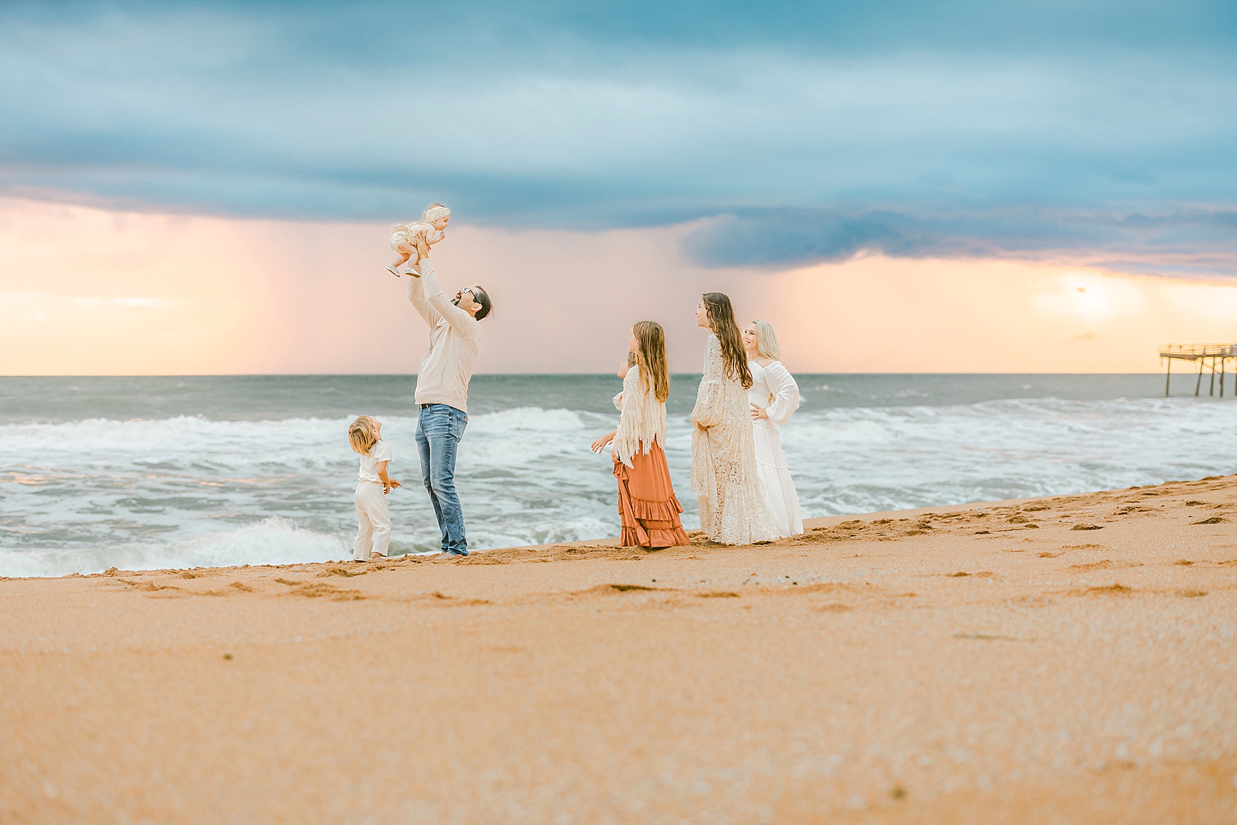 family playing together on flagler beach at sunrise against a stormy pastel colorful sky