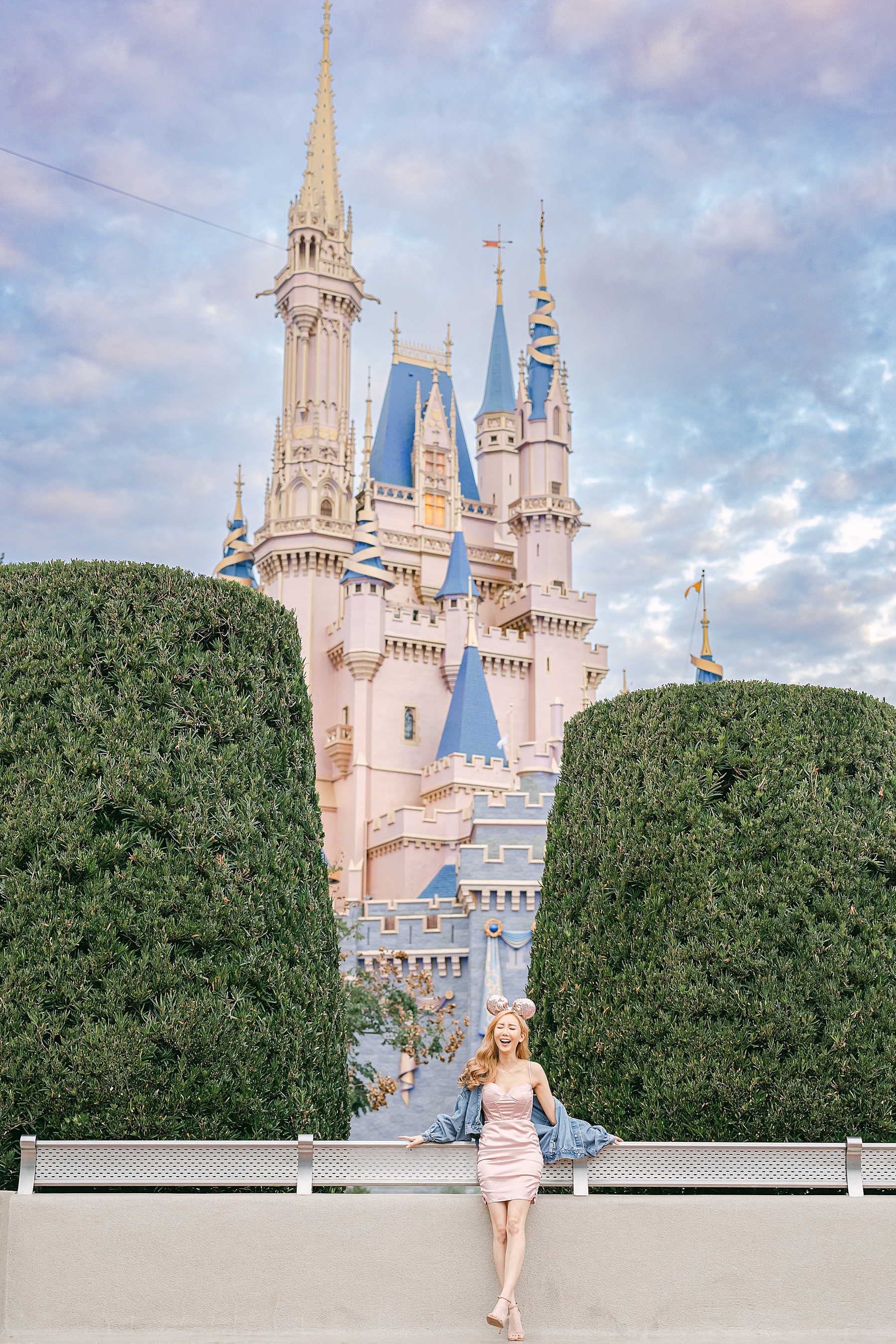 woman in fitted pink dress and jean jacket and heels outside of Cinderella's Castle at Magic Kingdom park