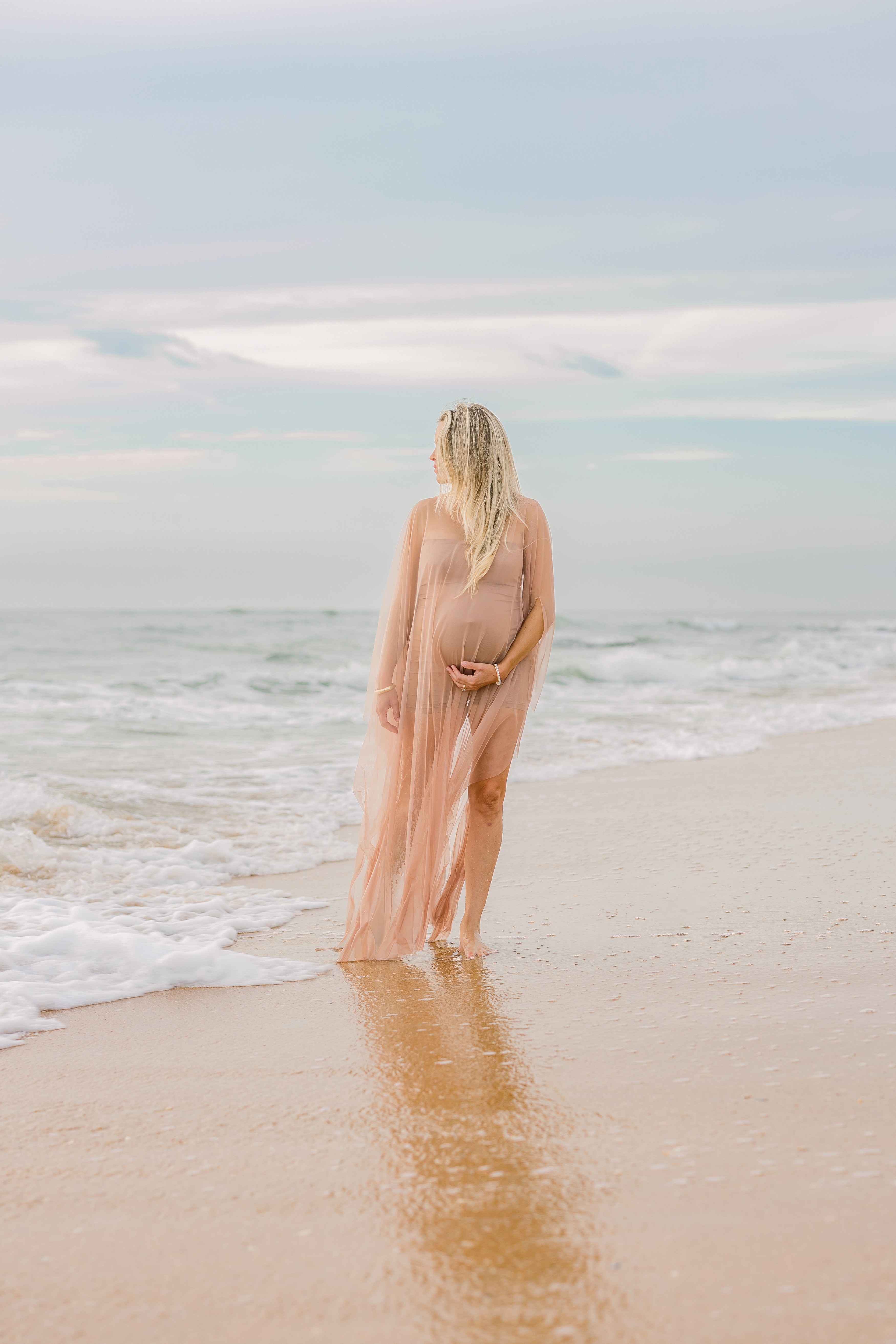 fine art maternity portrait of blond woman in sheer nude dress on the beach at sunrise