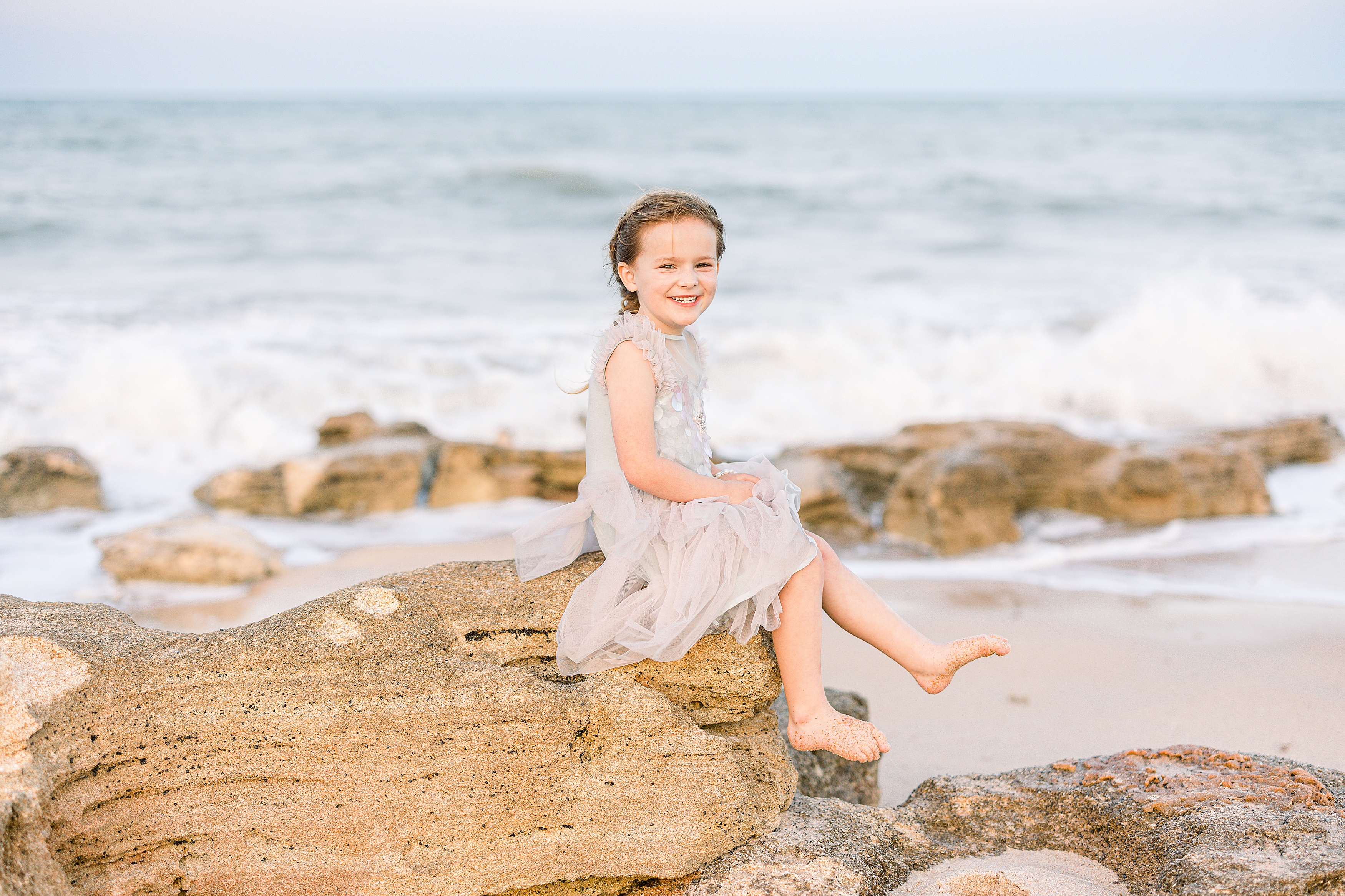 little girl in pastel mermaid tulle dress sitting on the rocks in Saint Augustine Beach
