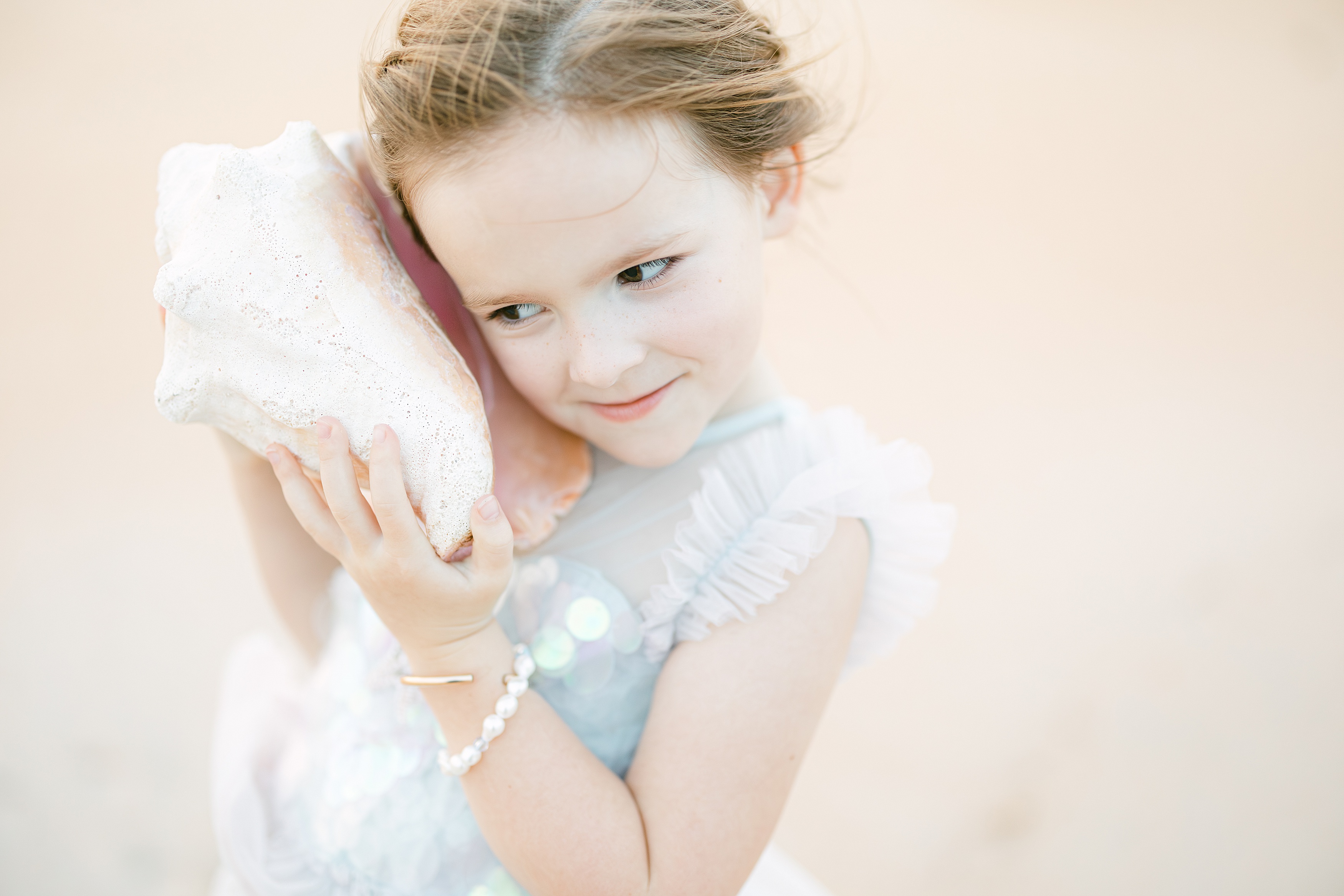 little girl holding a conch shell listening to the sounds of the ocean