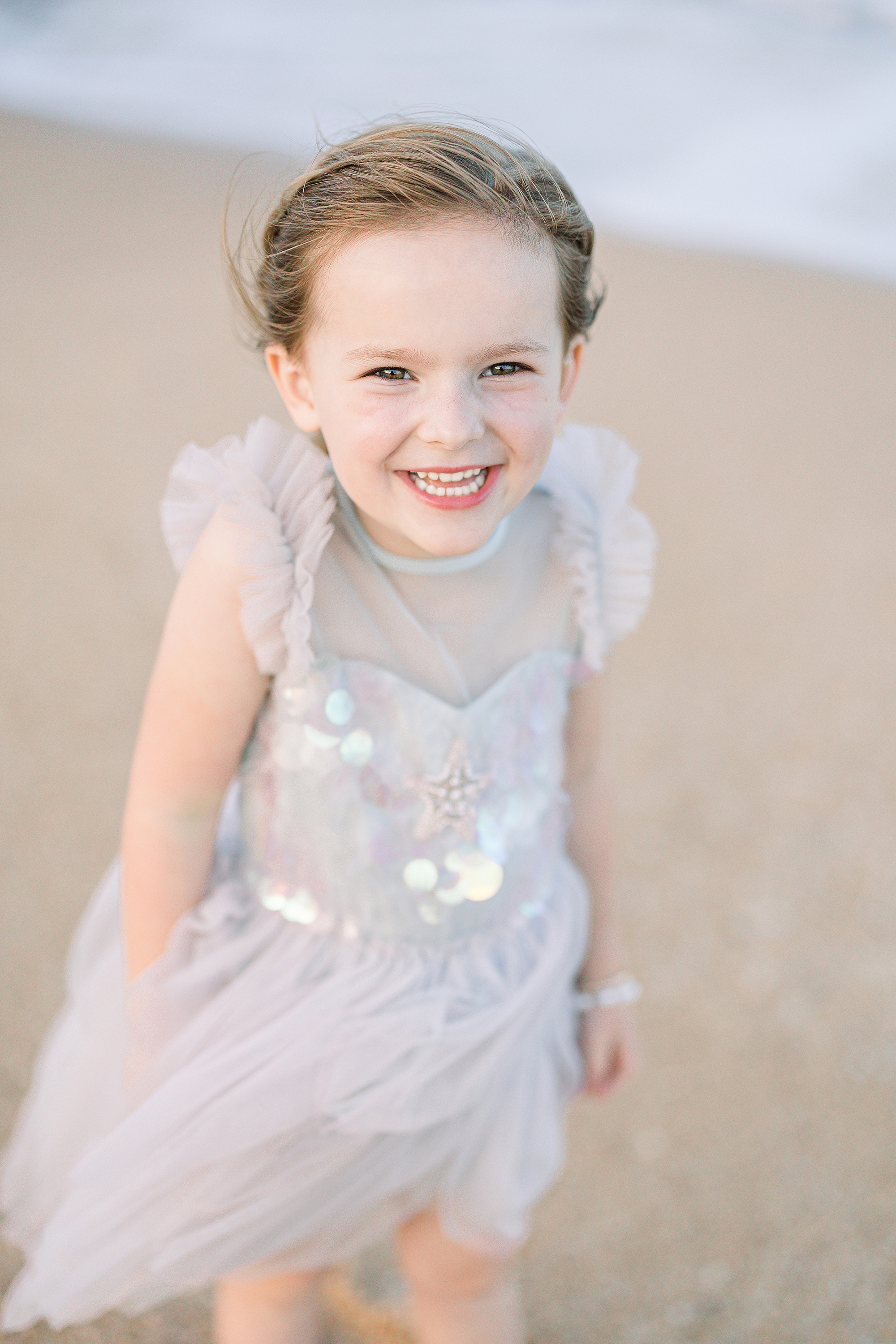 little girl laughing on the rocks at the beach during a pastel sunset