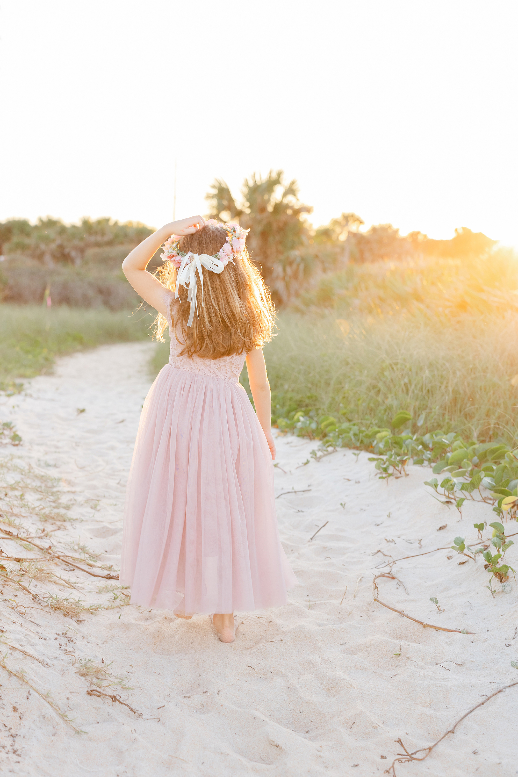 Sunlit portrait of a little girl in a flower crown and long pink skirt on the beach in St. Augustine.