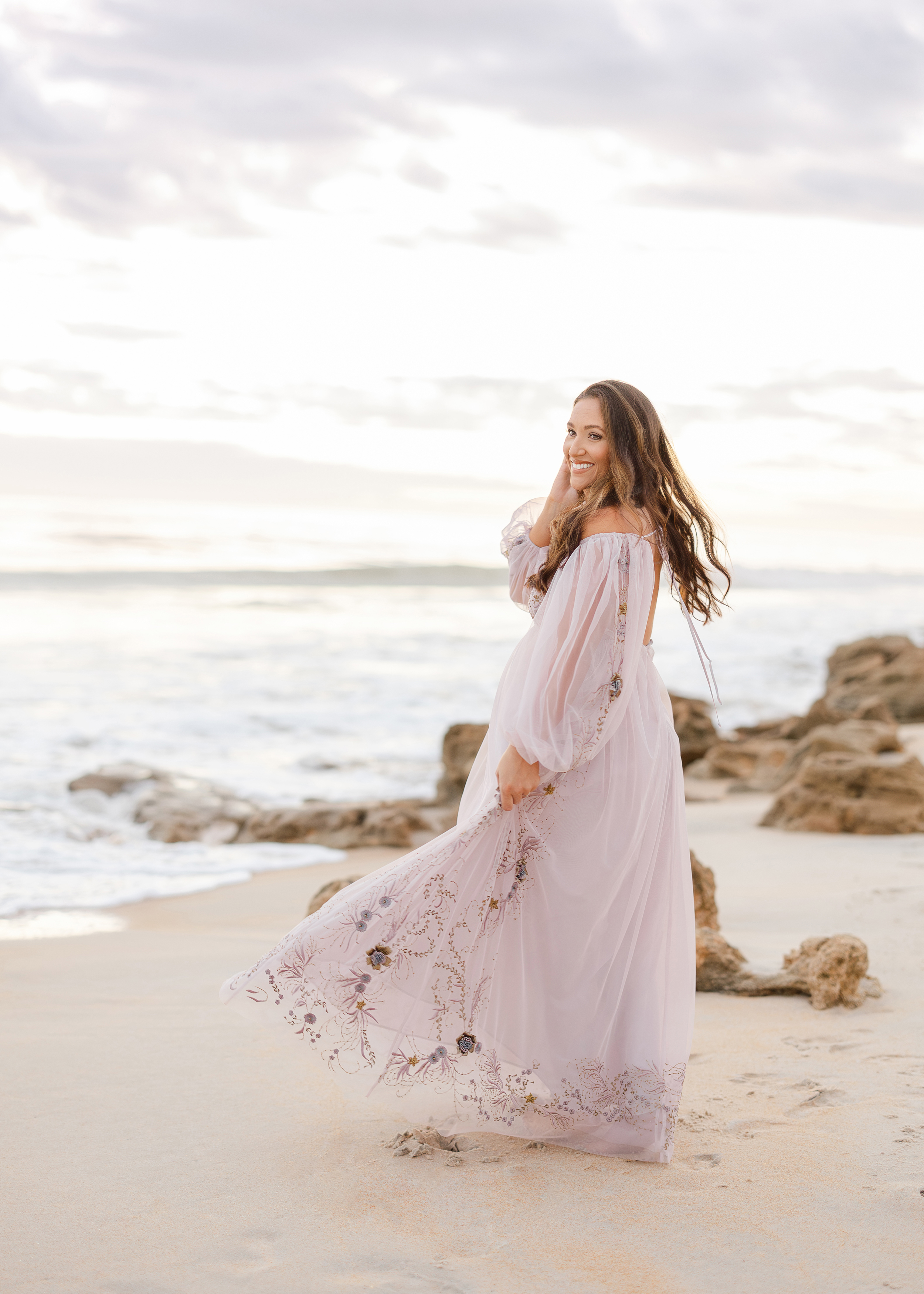 Light and airy maternity photo of a woman on the beach at sunrise.