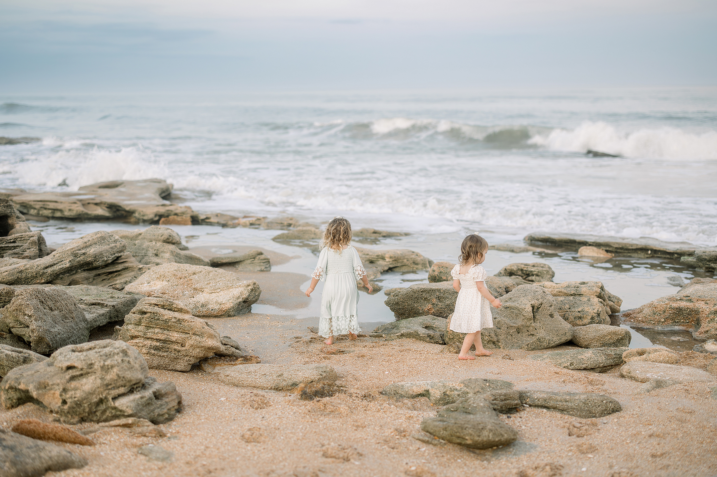 Two little girls standing on the rocks in St. Augustine Beach, Florida at sunset.