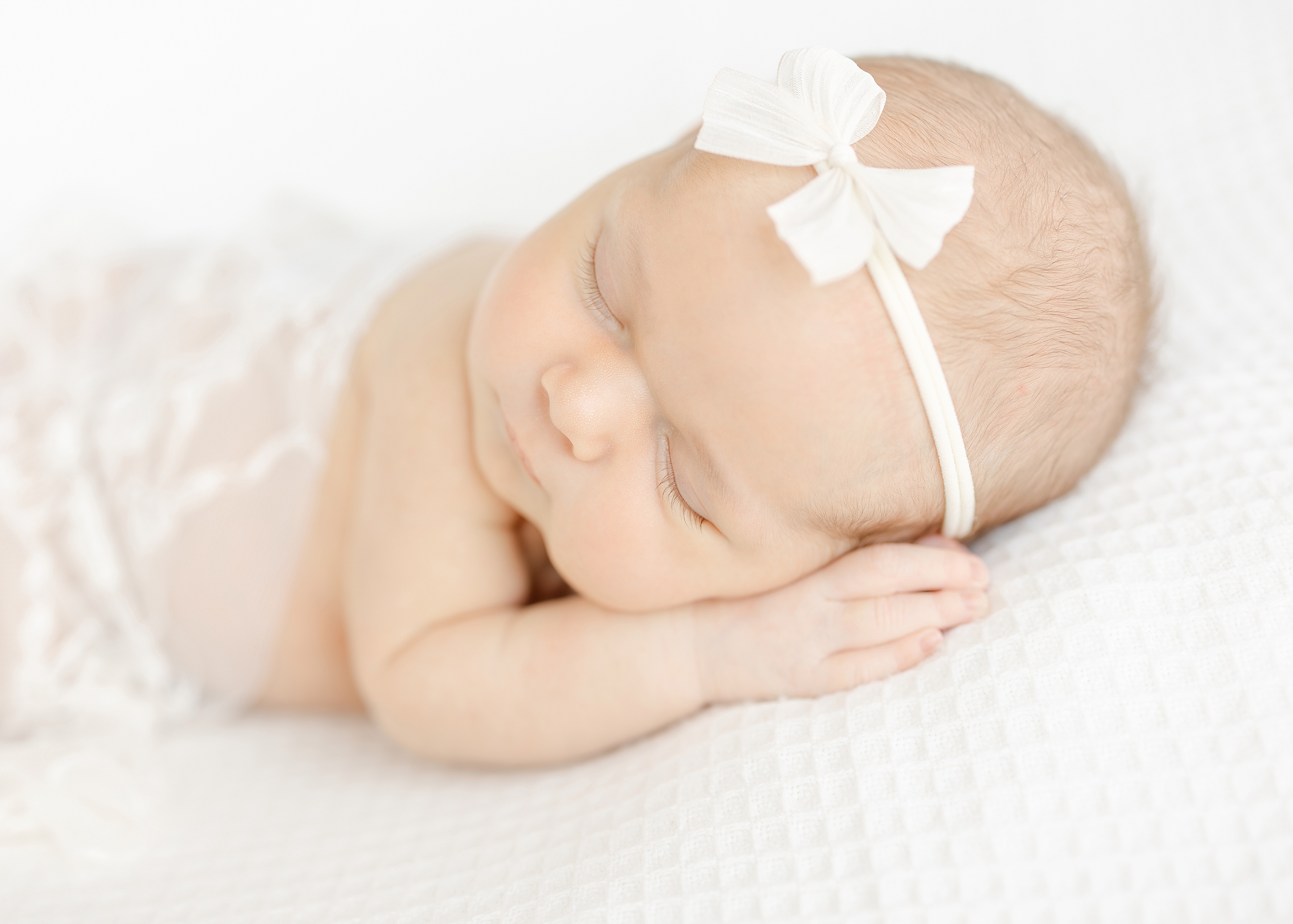 Light and airy newborn image of a baby girl in white lace and a white headband.